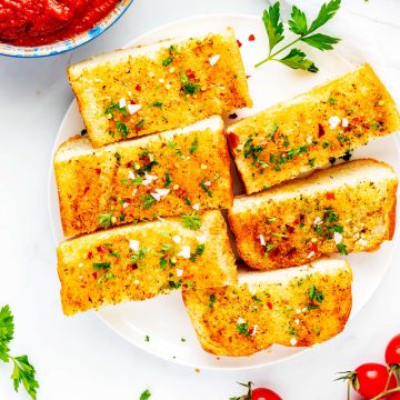 Square overhead photo of sliced air fryer garlic bread on a white plate with a small bowl of marinara next to it.