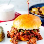 Square side photo of slow cooker sloppy joes on a bun garnished with parsley.