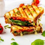 Square side photo of a pesto turkey panini on a white surface garnished with fresh basil.