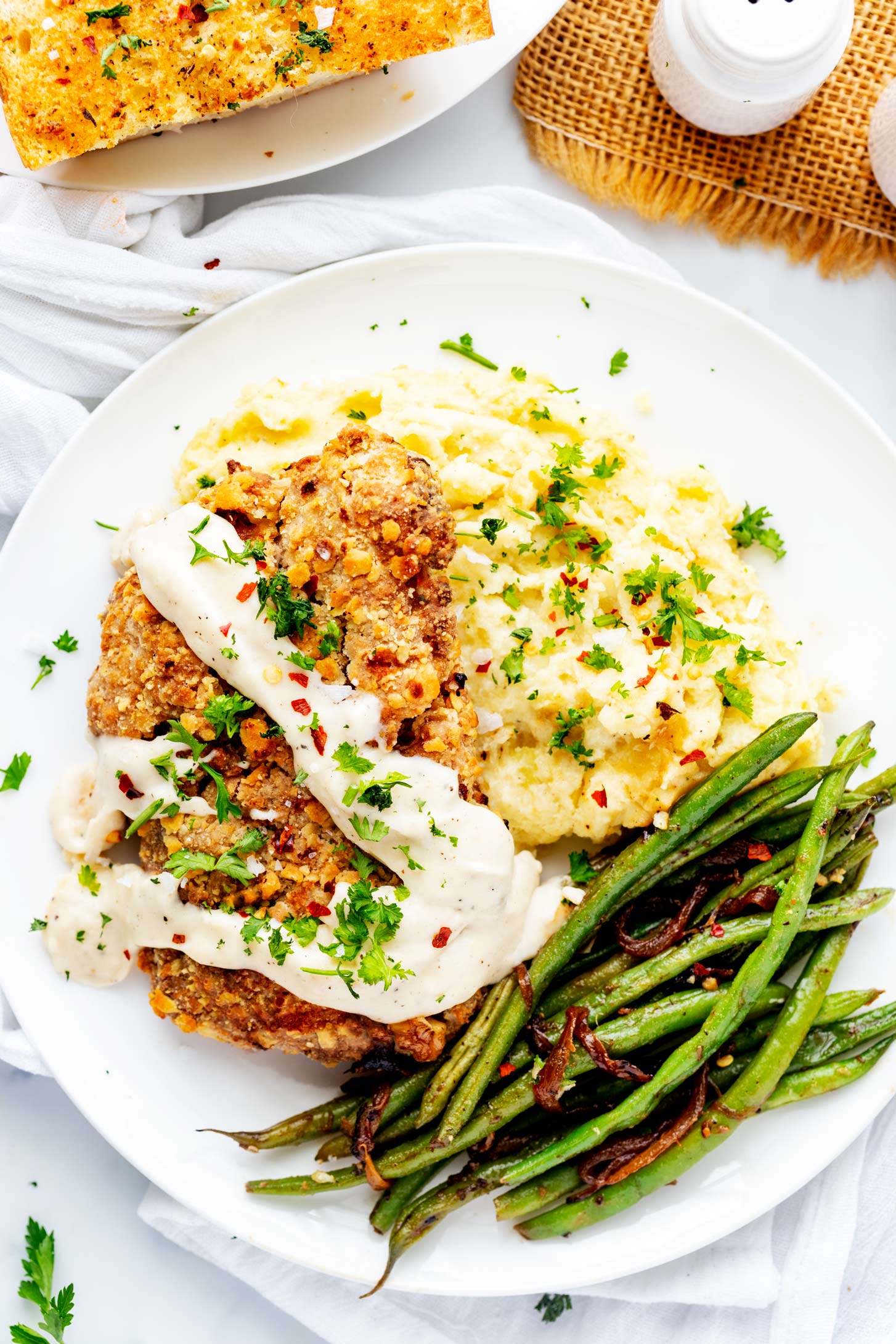 Overhead photo of a white plate with air fryer chicken fried steak and gravy over a bed of mashed potatoes with green beans.
