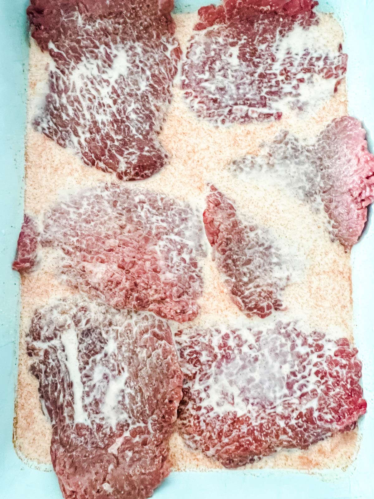 Cube steaks marinating in a mixture of milk, salt, paprika, and garlic powder.