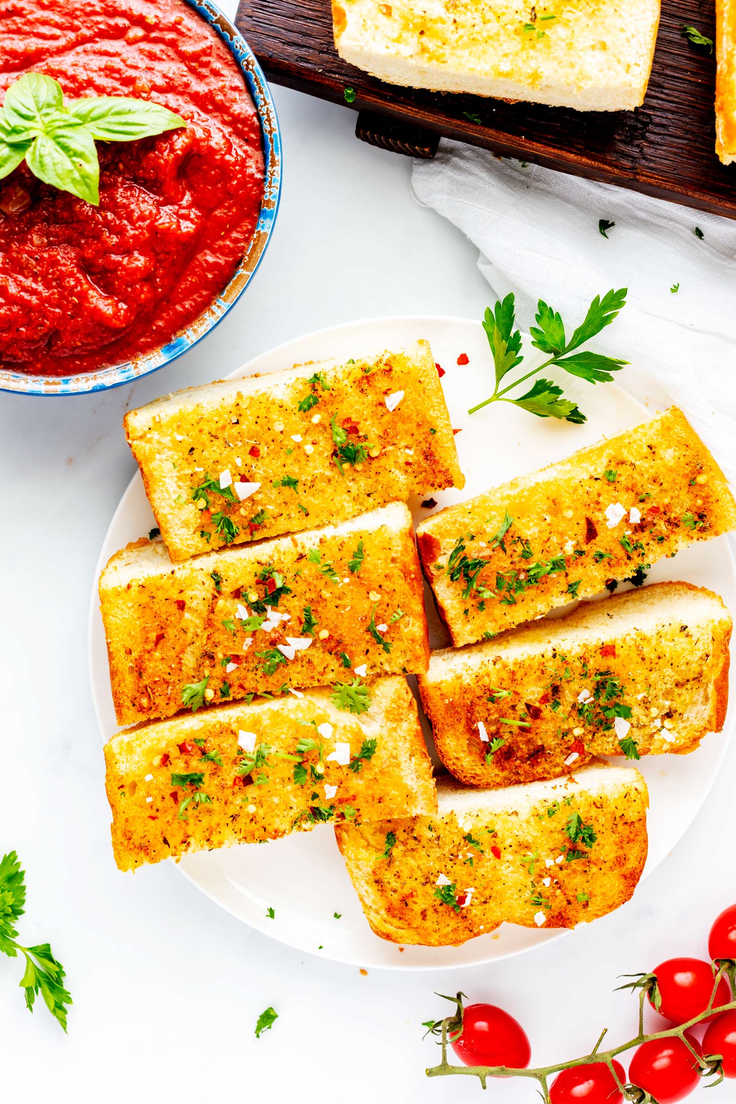 Overhead photo of sliced air fryer garlic bread on a white plate with a small bowl of marinara next to it.
