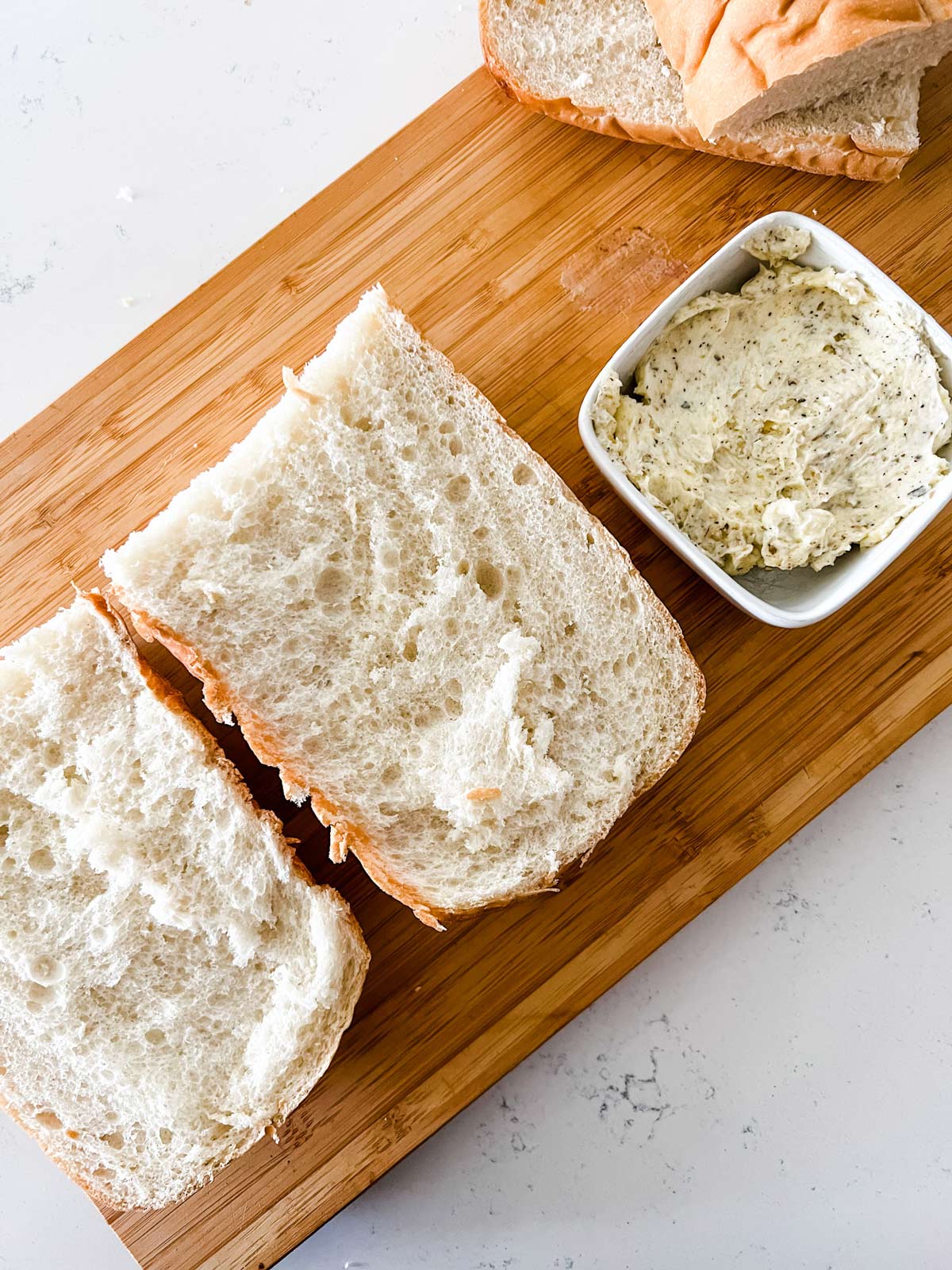 Garlic butter sitting next to sliced Italian bread on a cutting board.