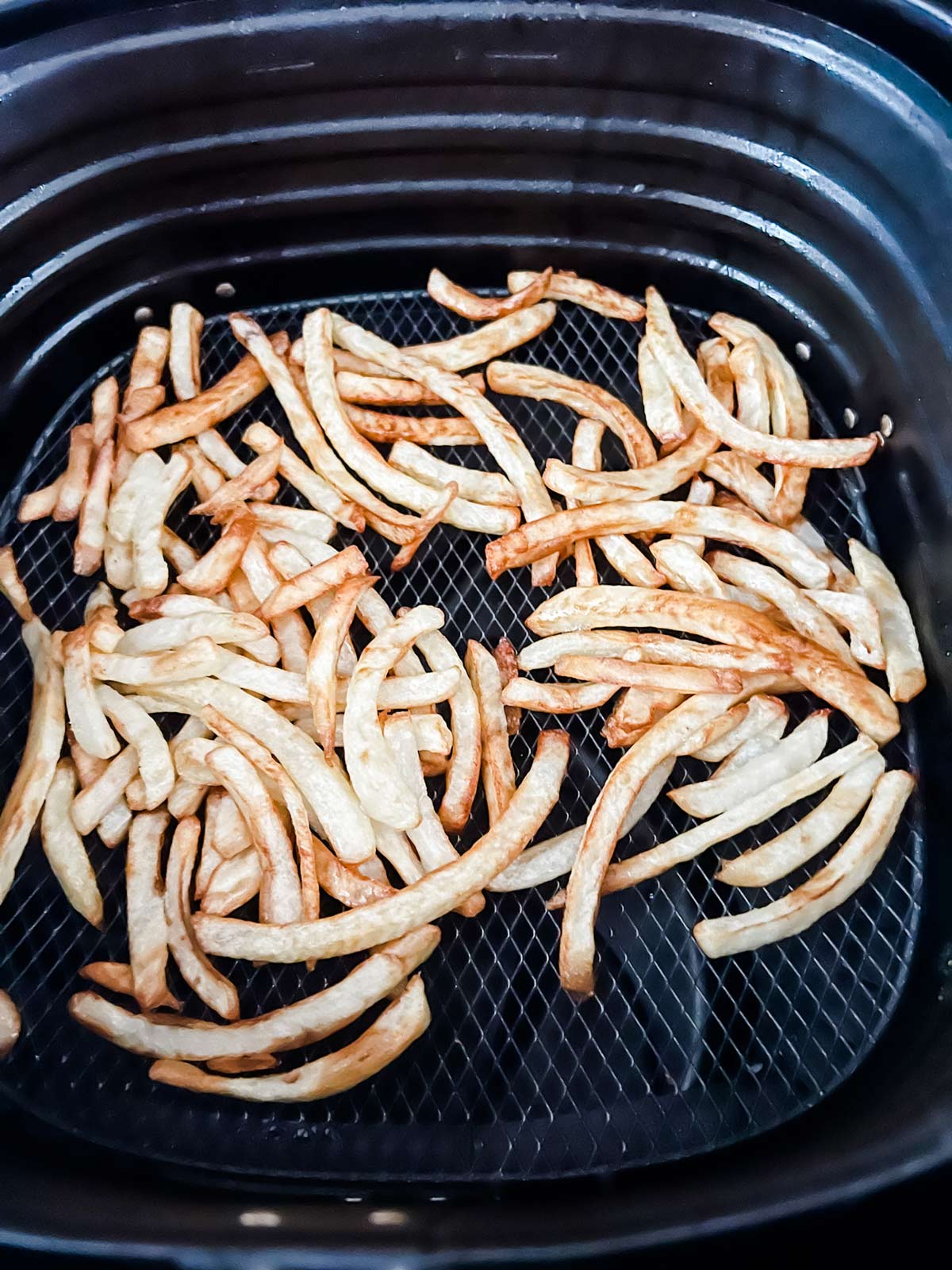 Partially cooked french fries in the basket of an air fryer.