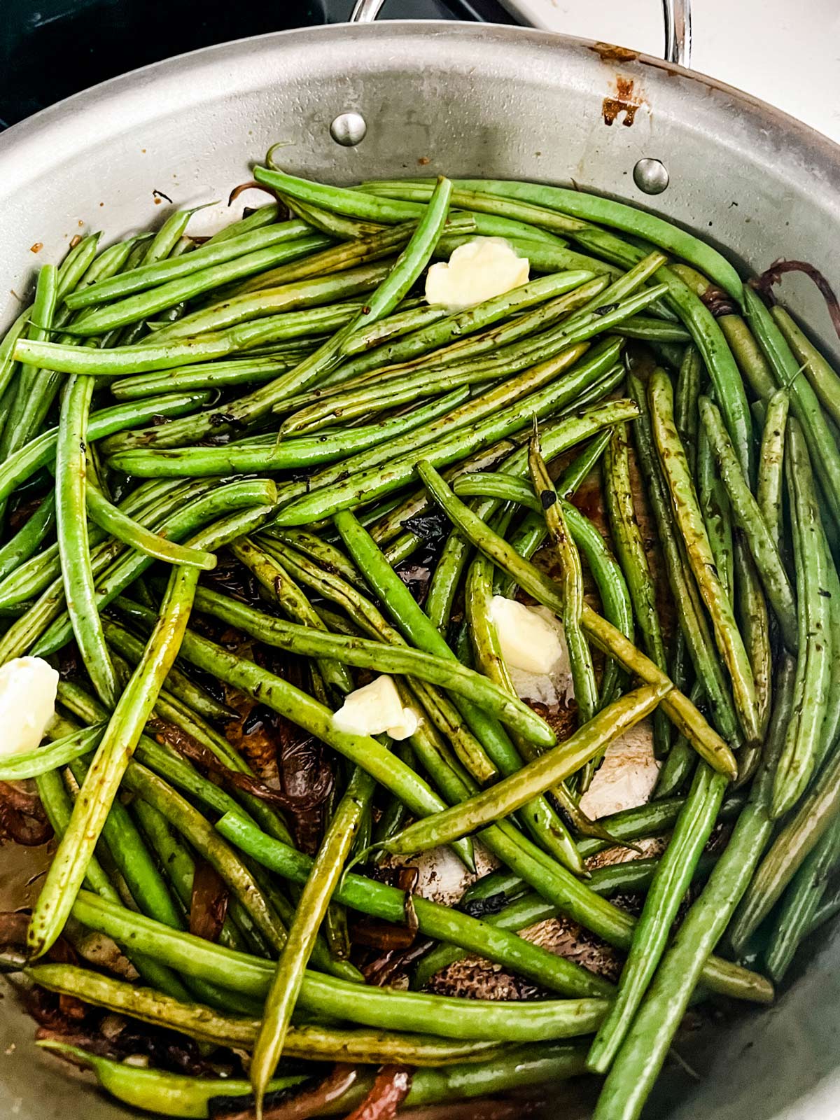 Green beans and butter added to a skillet with sauteed onion and garlic.