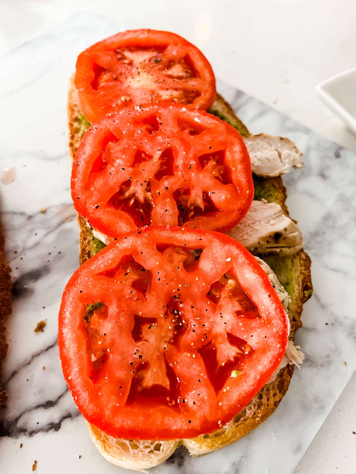 Pesto and sliced chicken topped with tomato on bread.