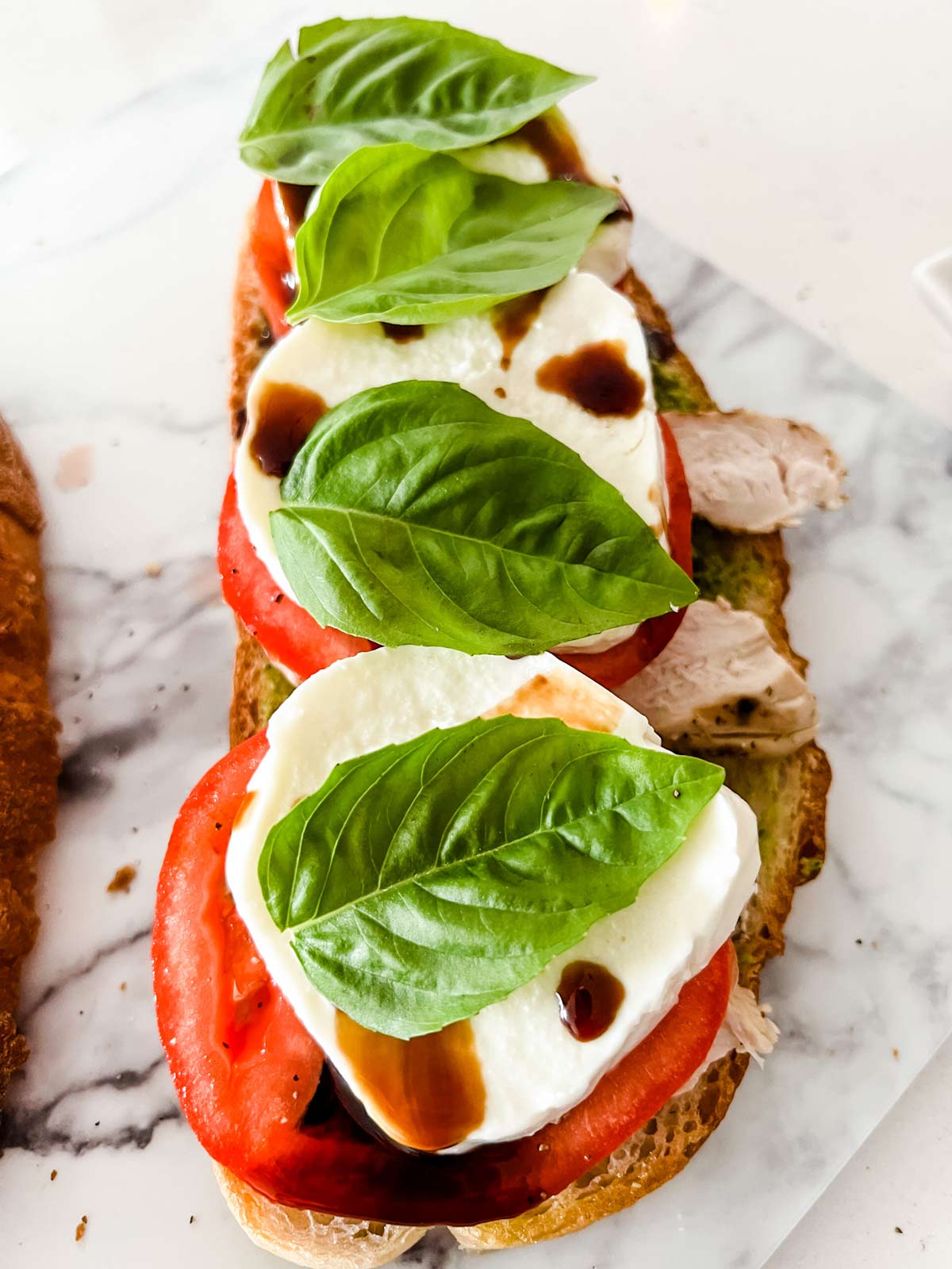 An open faced caprese chicken panini with basil on top ready to have the final piece of bread added.