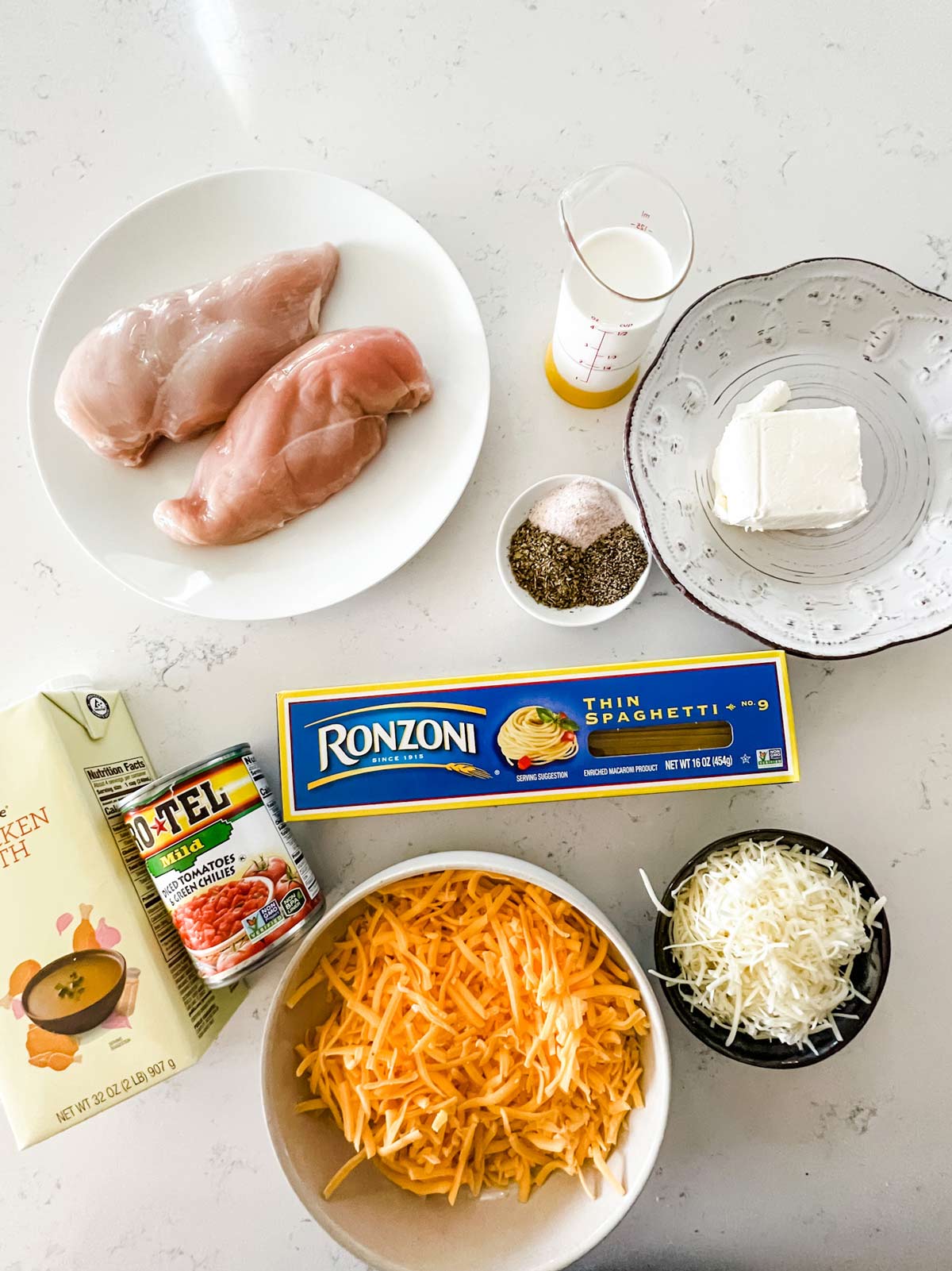 Overhead photo of chicken, spaghetti, broth, rotel, cream cheese, cream, seasonings, and cheese.