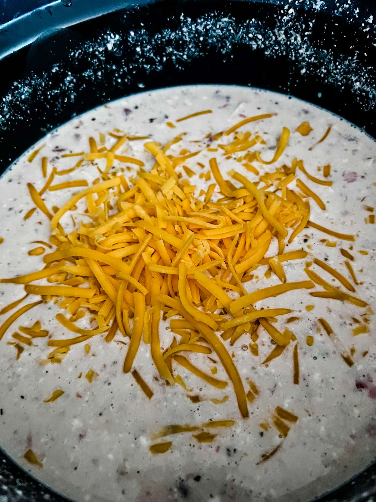 Cheese being whisked into a cream sauce in a slow cooker.