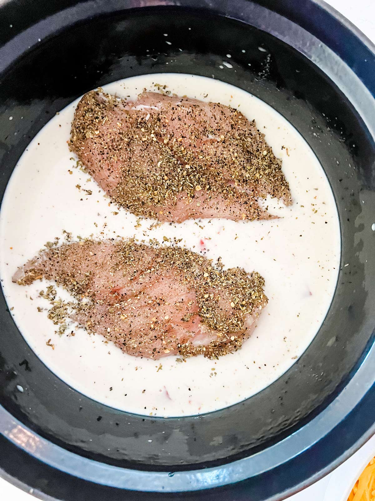 Chicken on top of a cream sauce in a slow cooker.