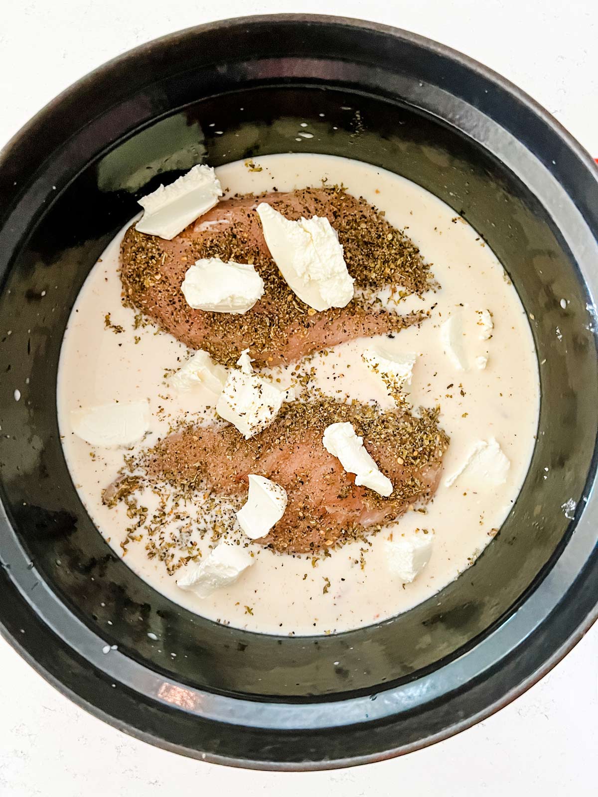Cream cheese on top of chicken and a cream sauce in a slow cooker.