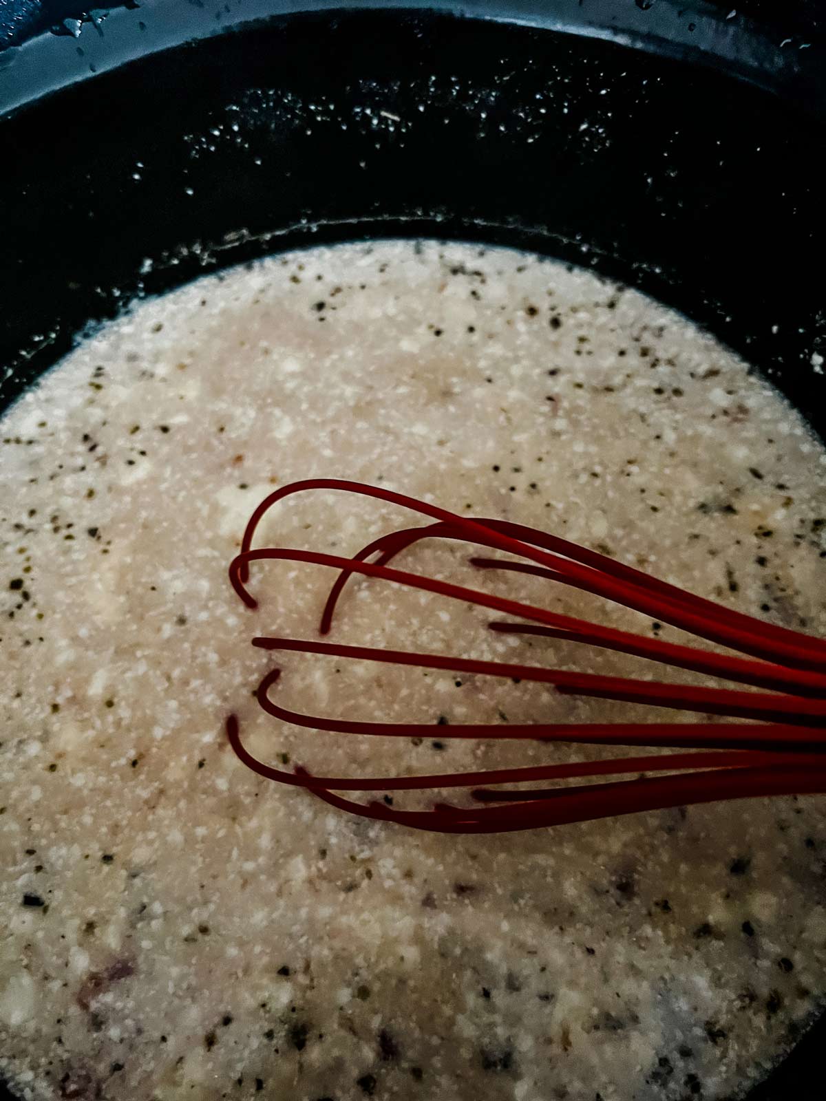 A whisk mixing up sauce for chicken spaghetti in a slow cooker.