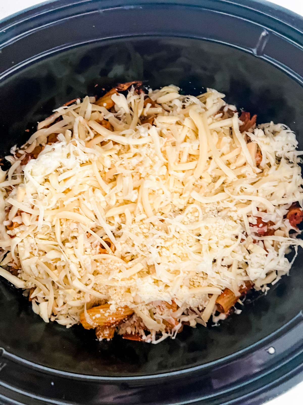 Crockpot pizza casserole with cheese on top of it in a slow cooker ready to cook.