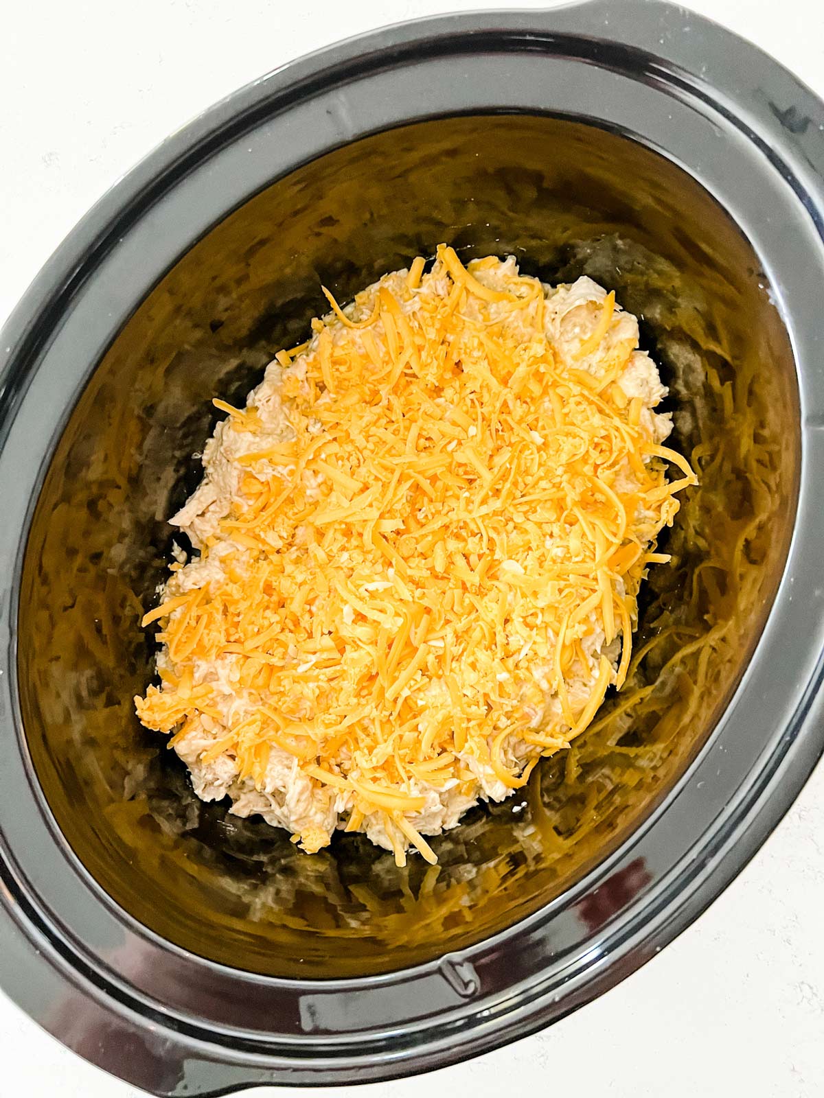 Ranch chicken in the crockpot with shredded cheese on it ready to melt.