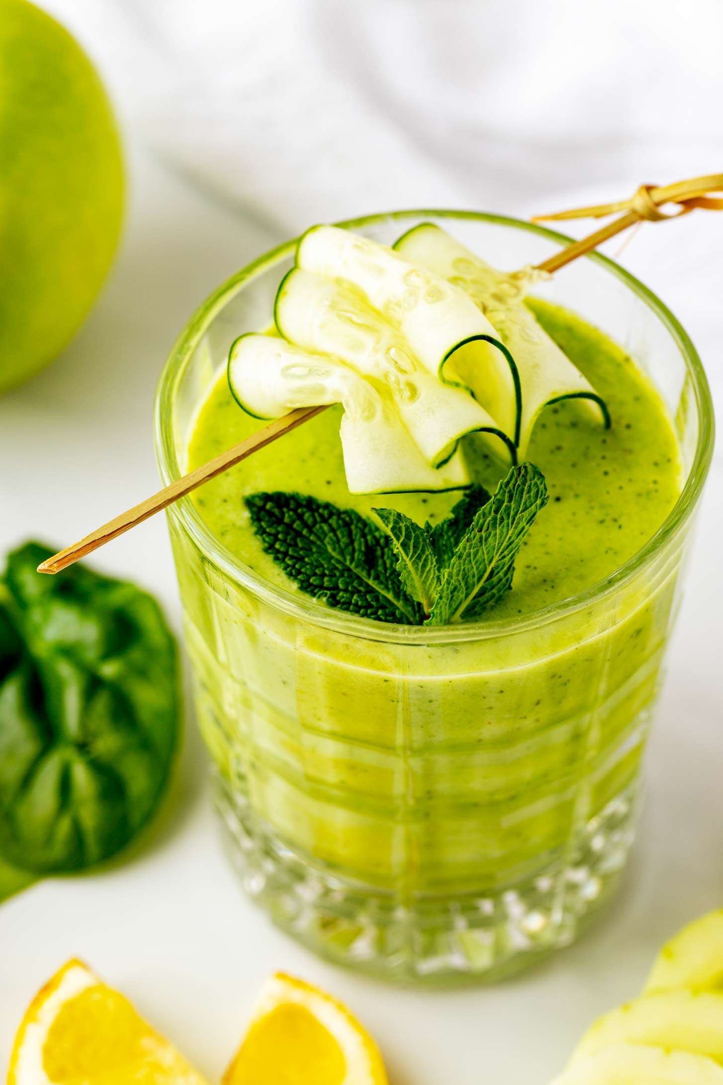 Photo of a small glass with a cucumber apple smoothie garnished with mint and cucumber.