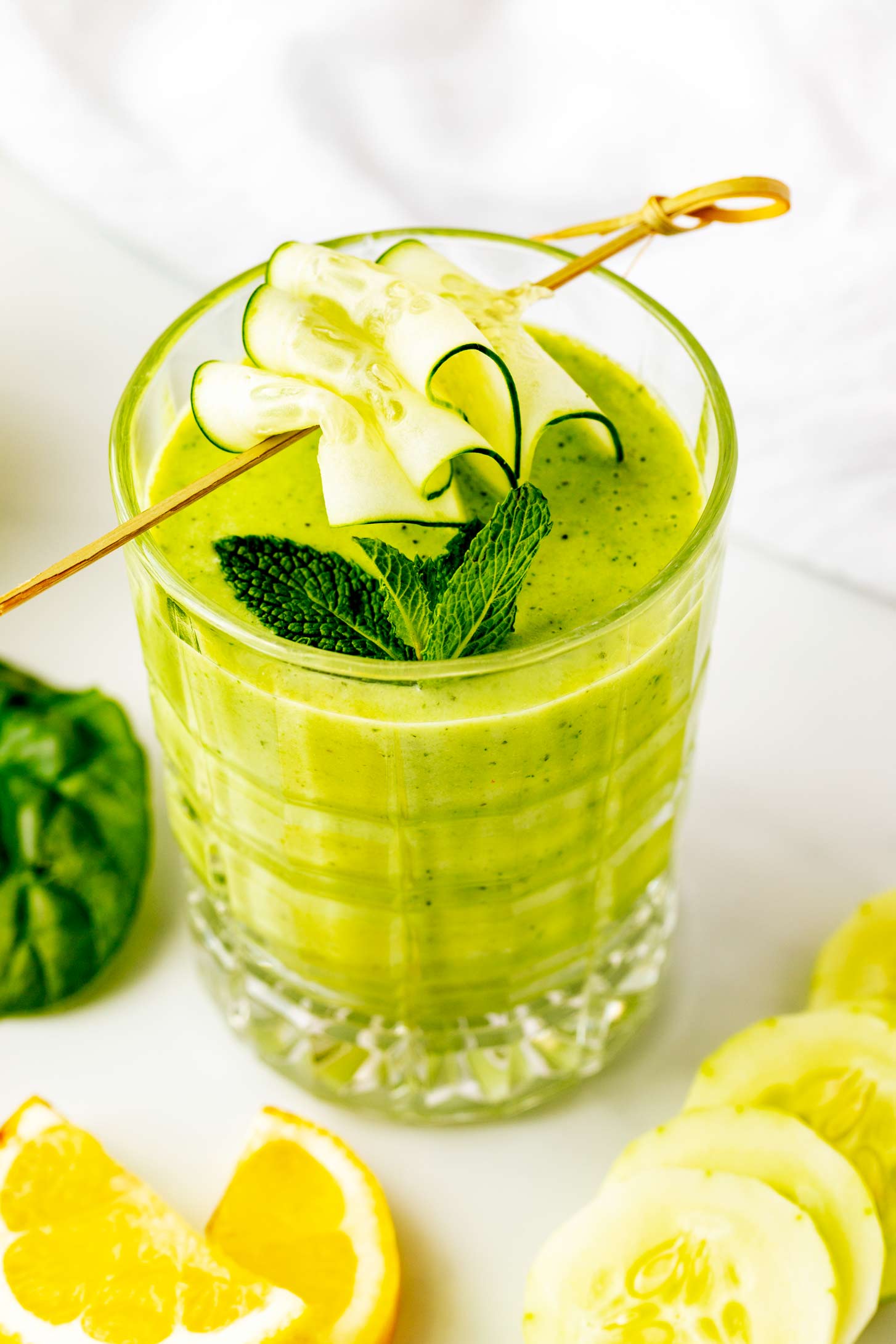 Side photo of a cucumber apple smoothie surrounded by apple, spinach and lemon.