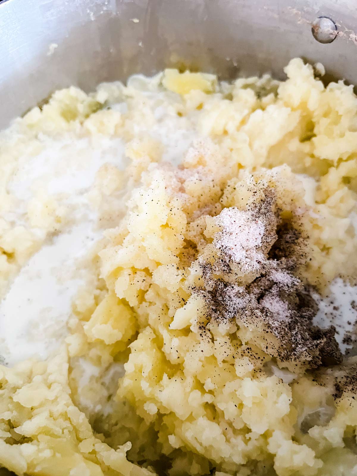 Seasonings and cream being added to mashed potatoes.