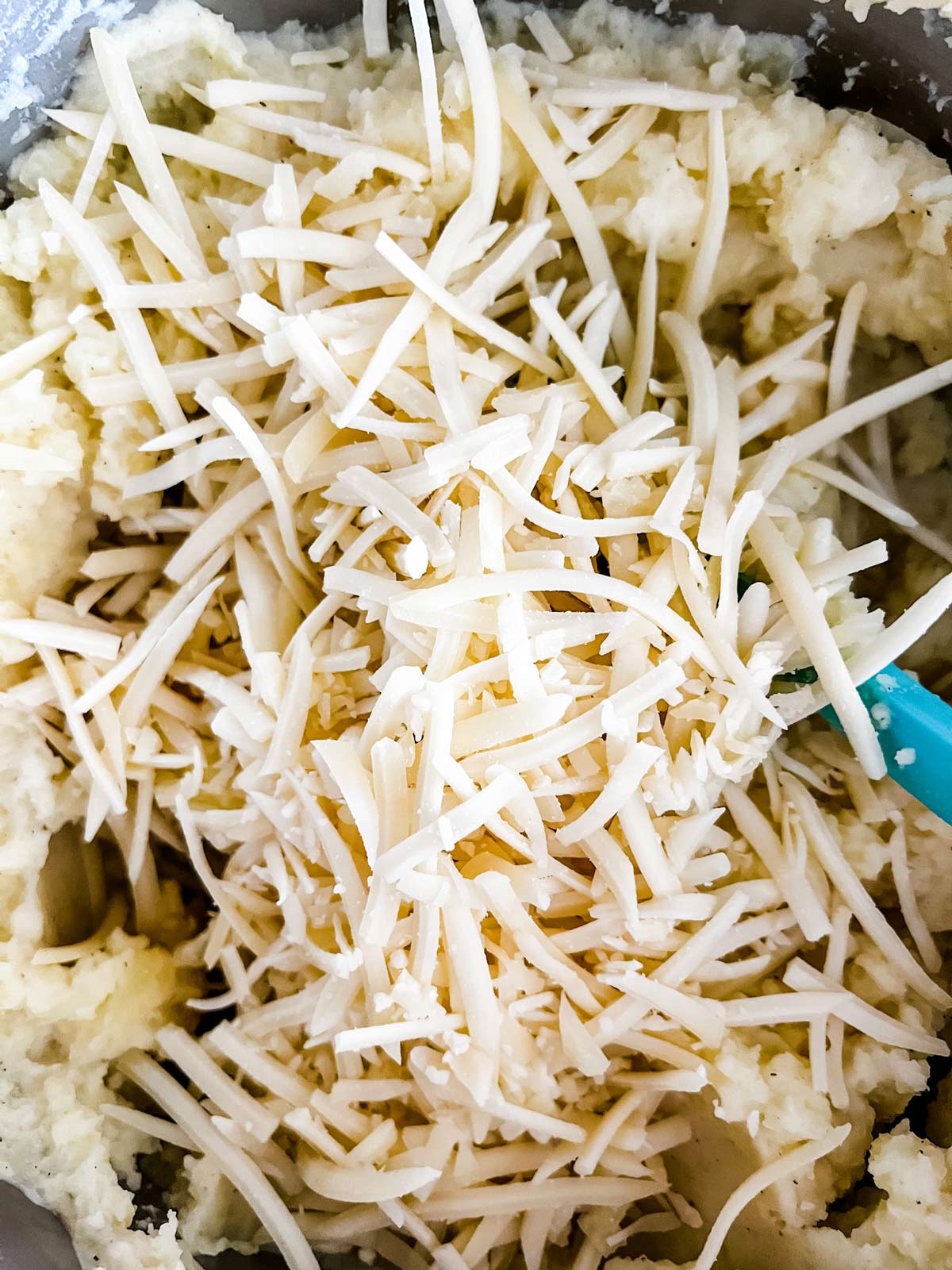 Shredded cheese being stirred into potatoes.