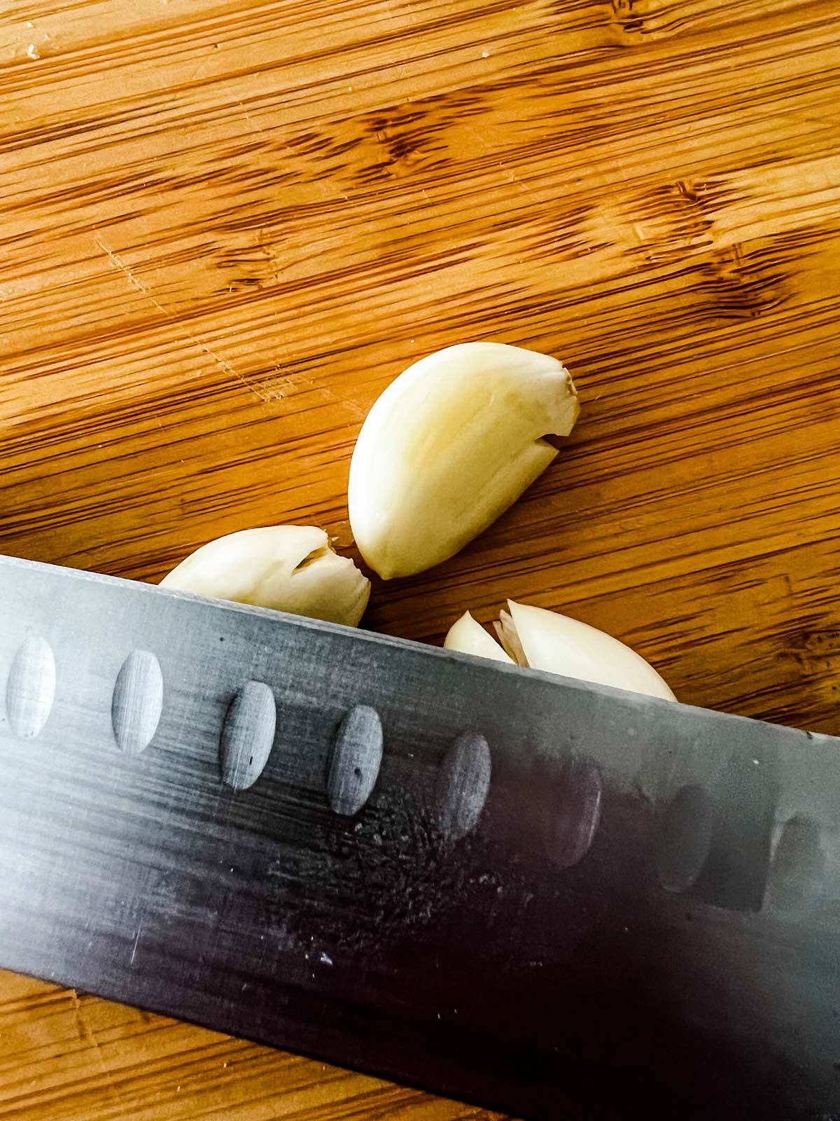 Garlic being crushed with the side of a knife.