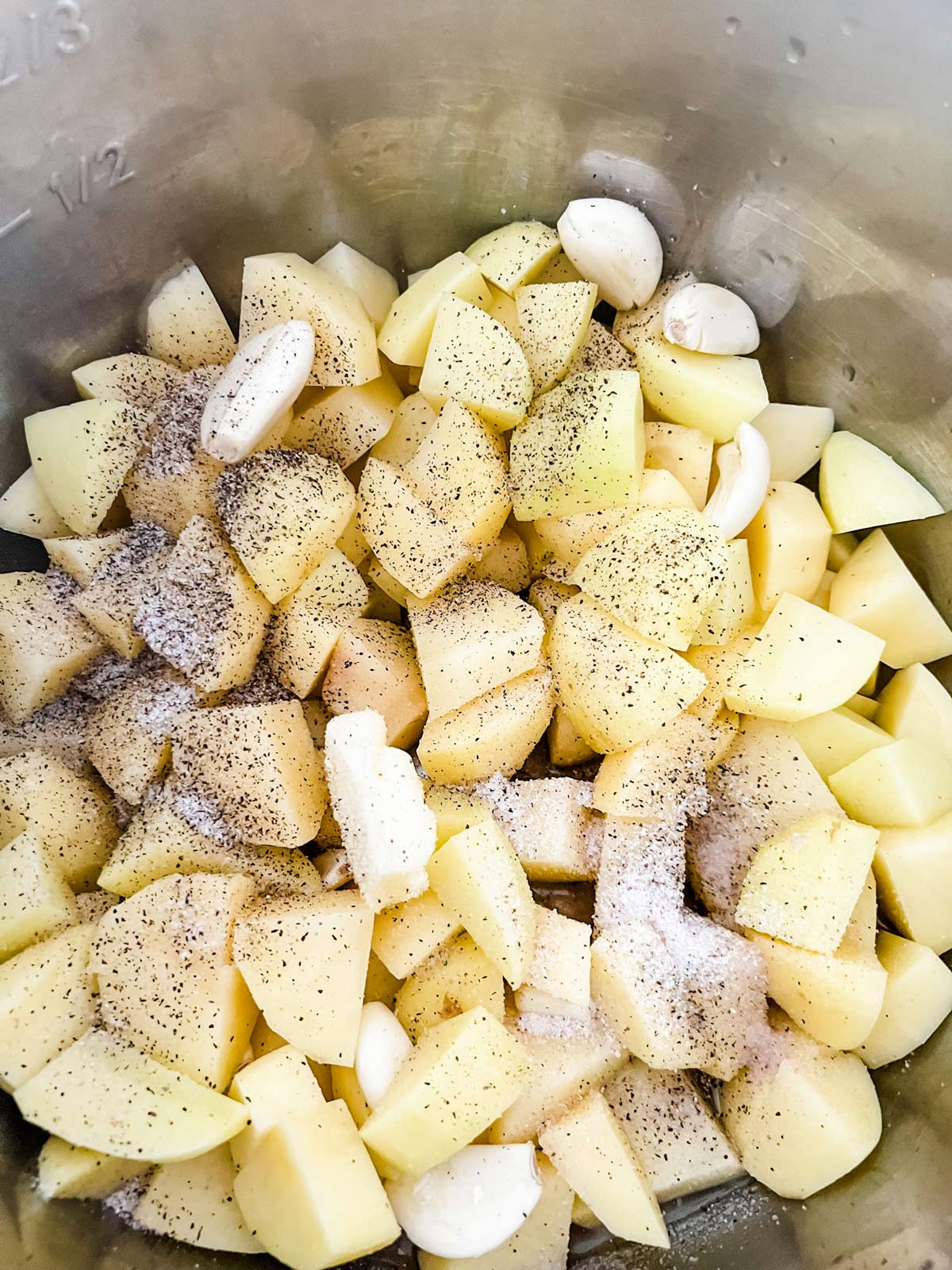 Overhead photo of potatoes, smashed garlic, butter, salt and pepper in the inner pot of an Instant Pot.