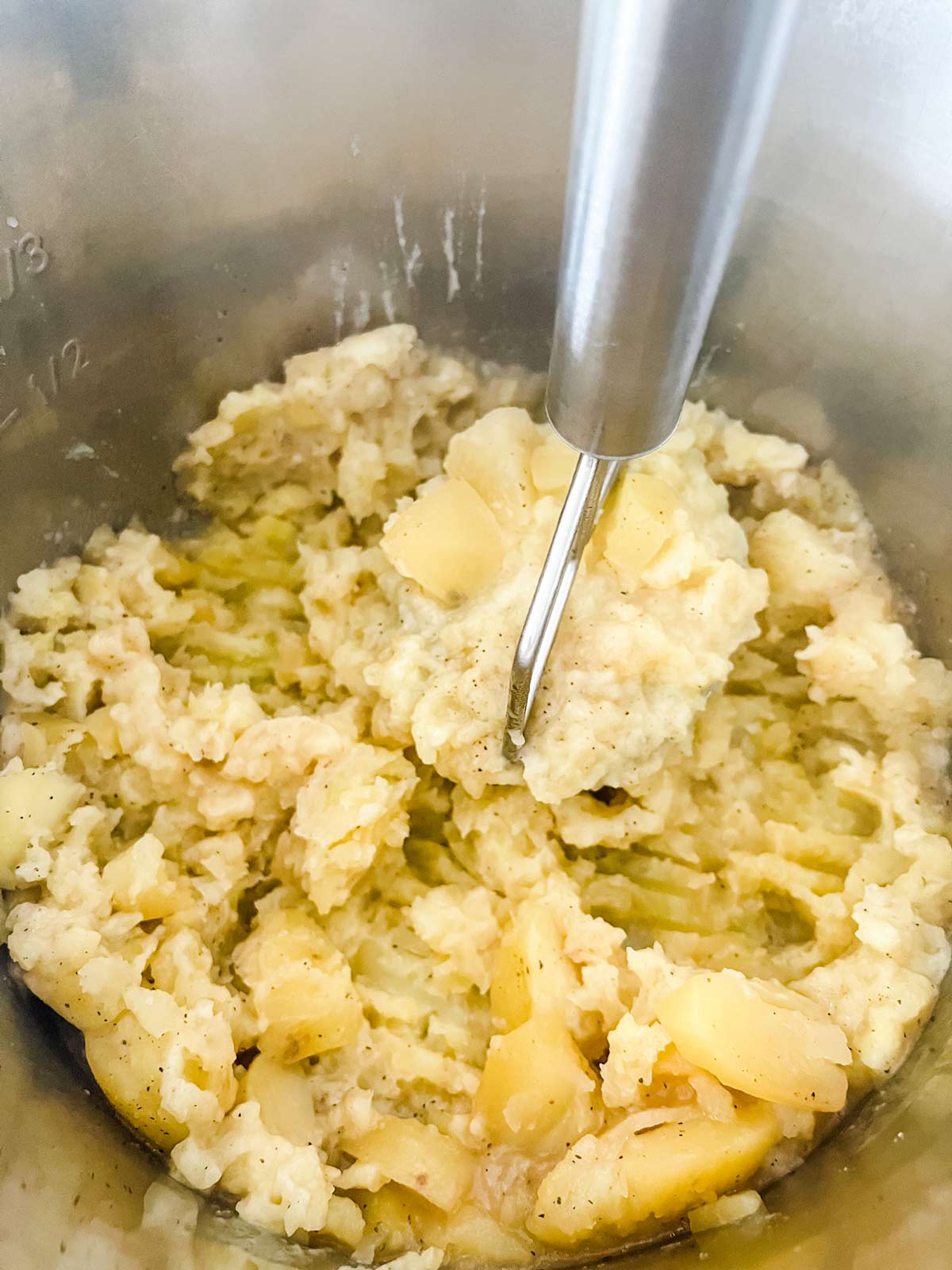 Potatoes being mashed in the inner pot of an Instant Pot.