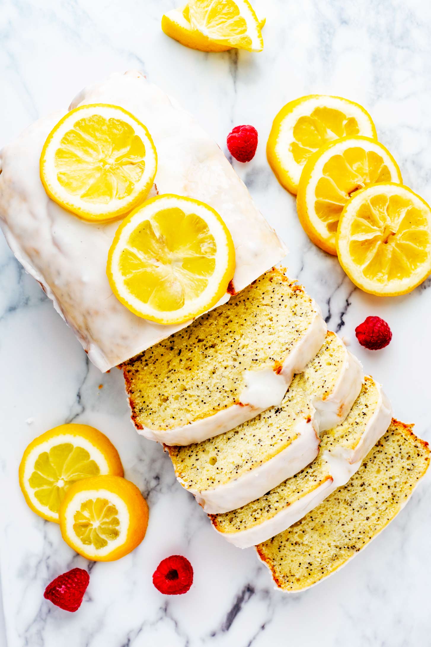 Overhead photo of a glazed lemon loaf garnished with candied lemons on a white board.