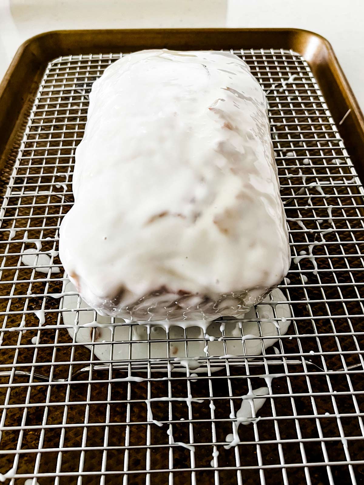 A glazed lemon loaf on a cooling rack set on top of a baking sheet.