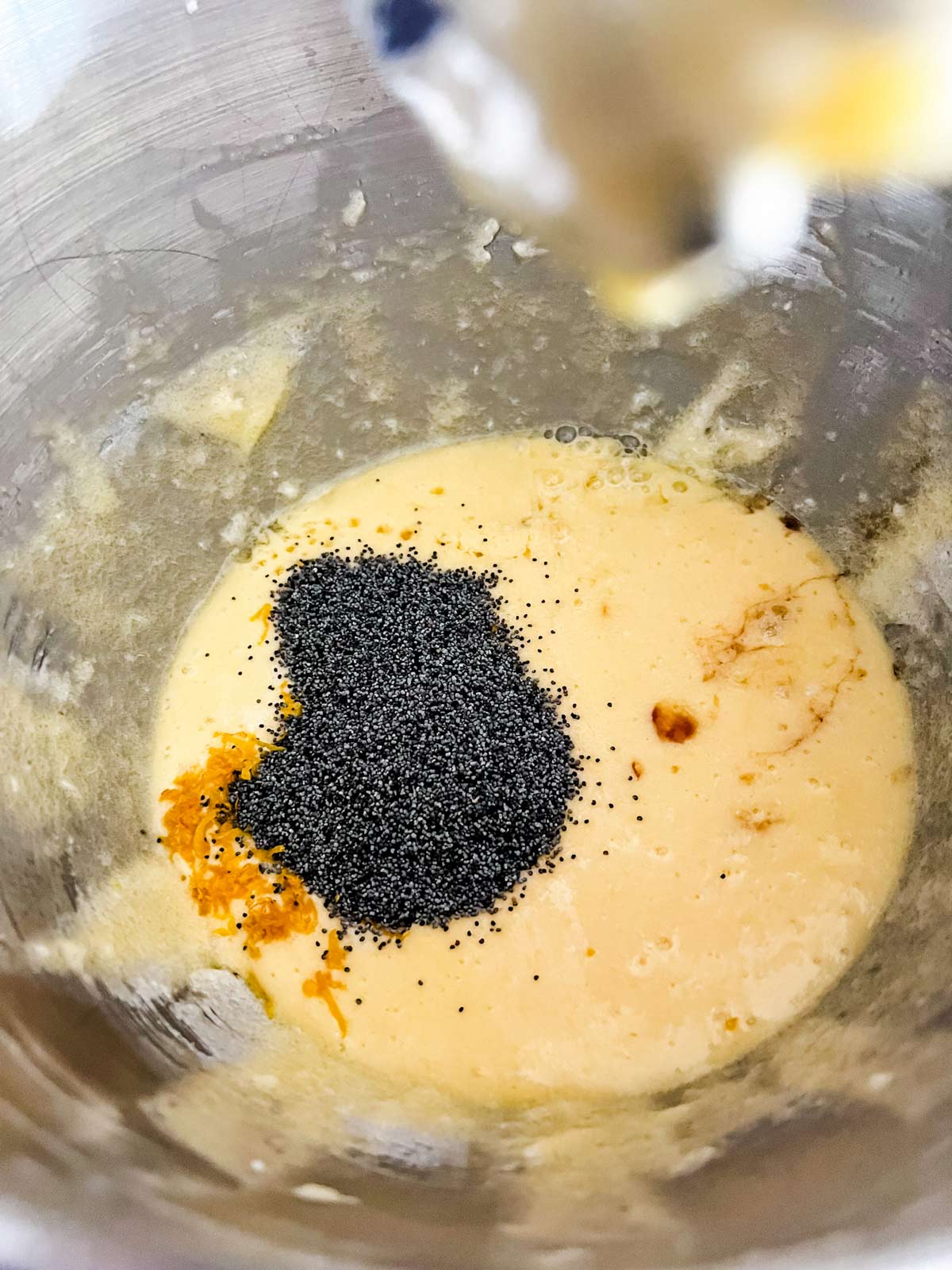  lemon juice, zest, vanilla extract, and poppy seeds being added to eggs, butter, and sugar.