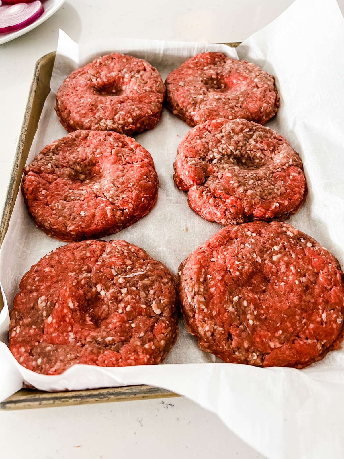 Burger patties on a sheet pan with a small indent.