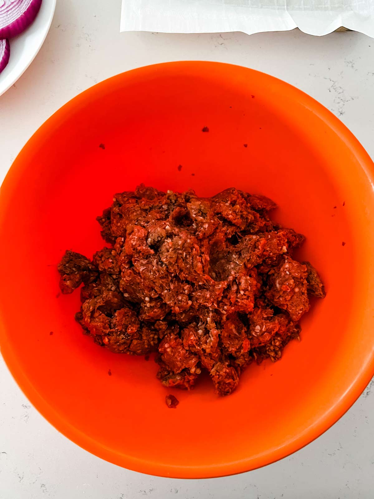 Ground beef and seasonings being mixed together in an orange bowl.