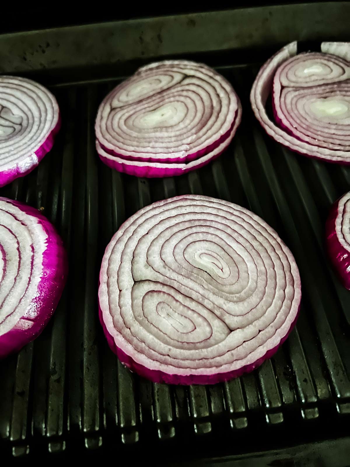 Sliced red onion cooking on a Ninja Foodi grill.