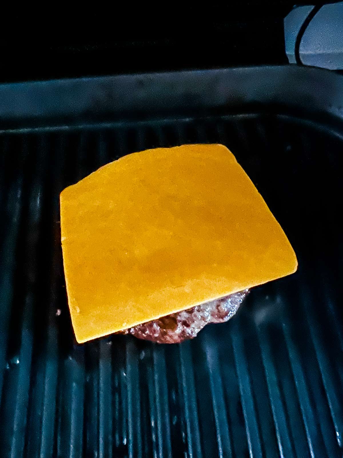 Cheese on top of a burger on a Ninja Foodi grill.