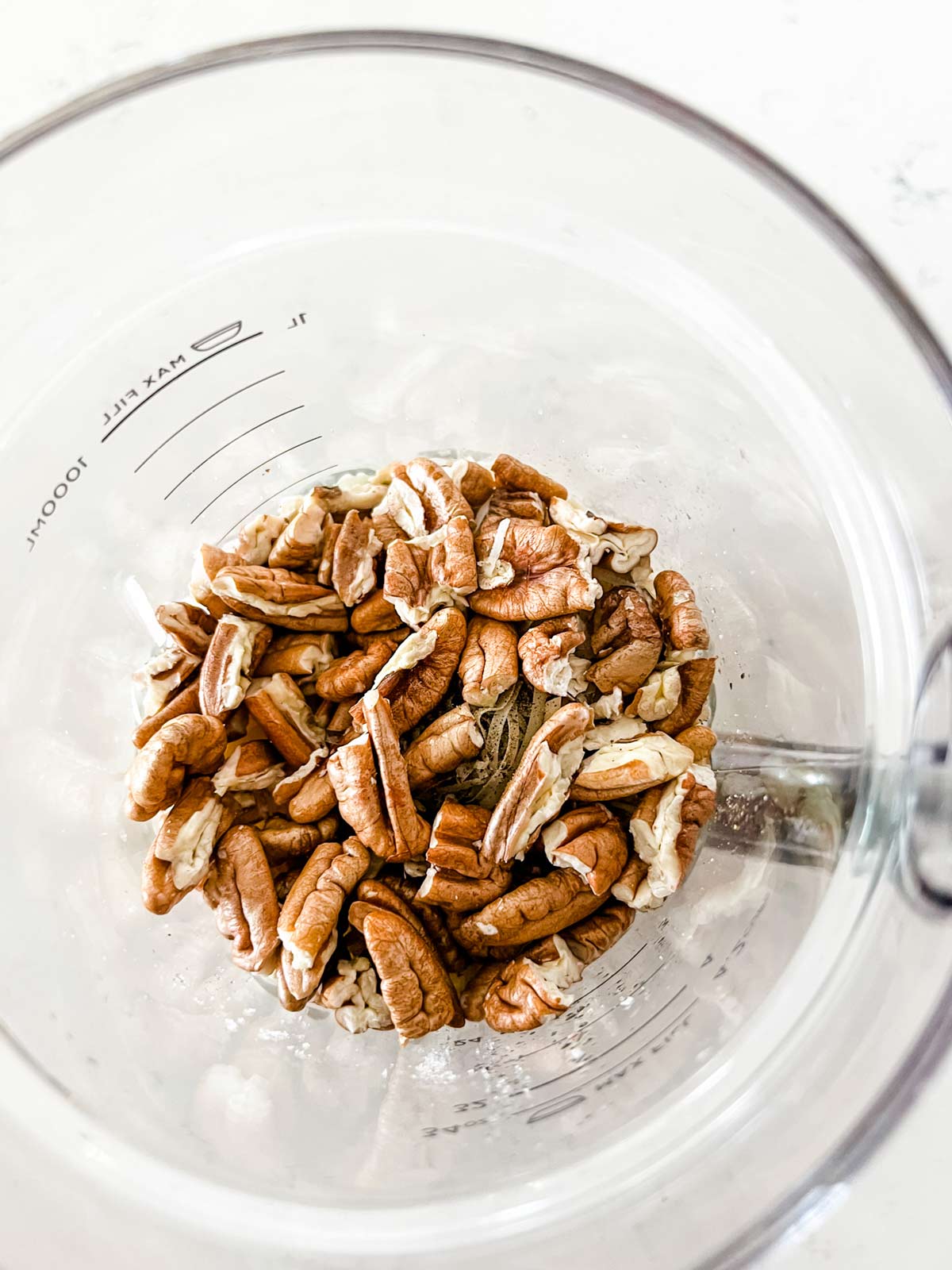 Pecans on top of other pesto ingredients in a blender.