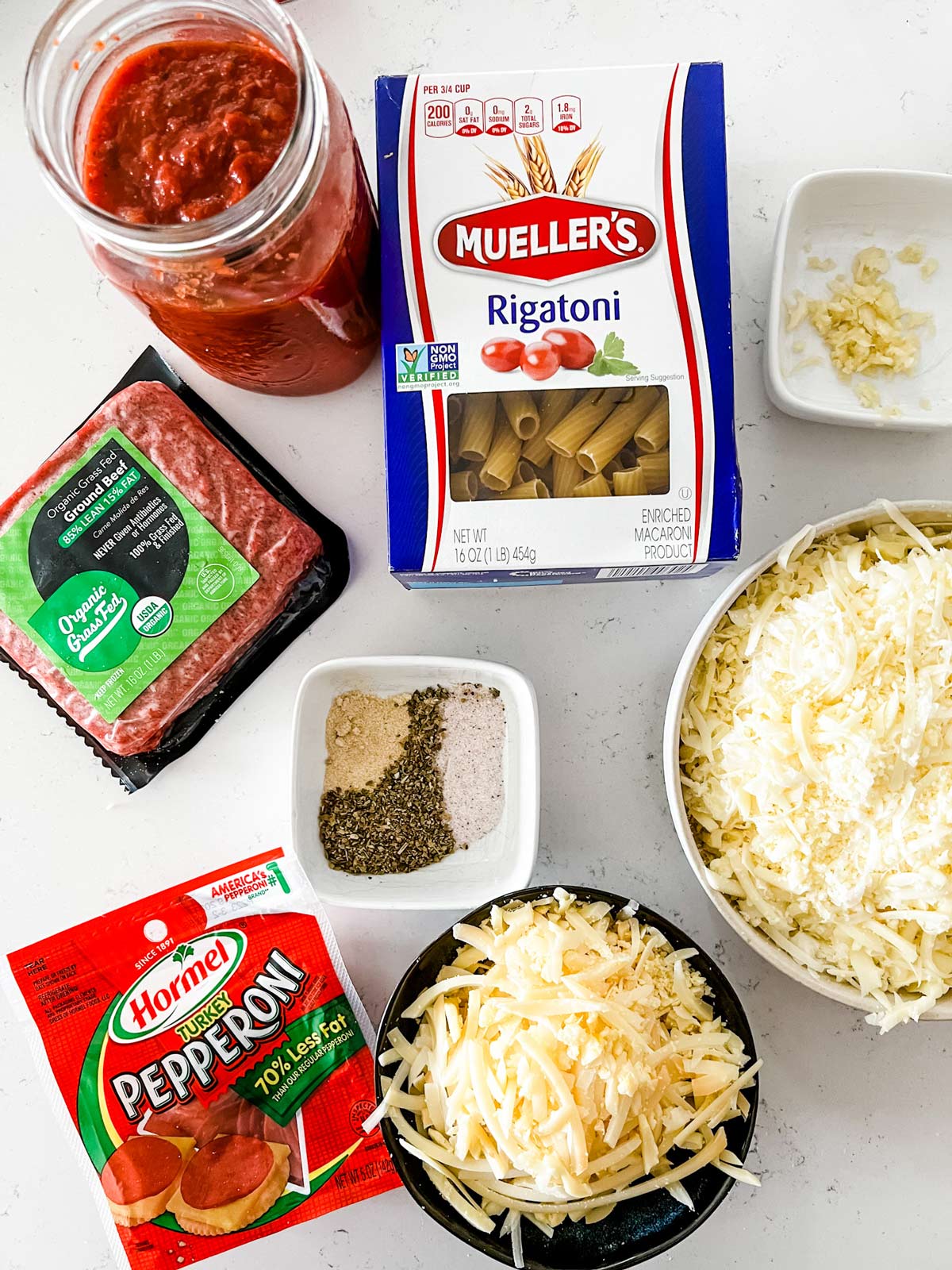 Overhead photo of pasta, marinara, ground beef, pepperoni, shredded cheeses, garlic, and seasonings.