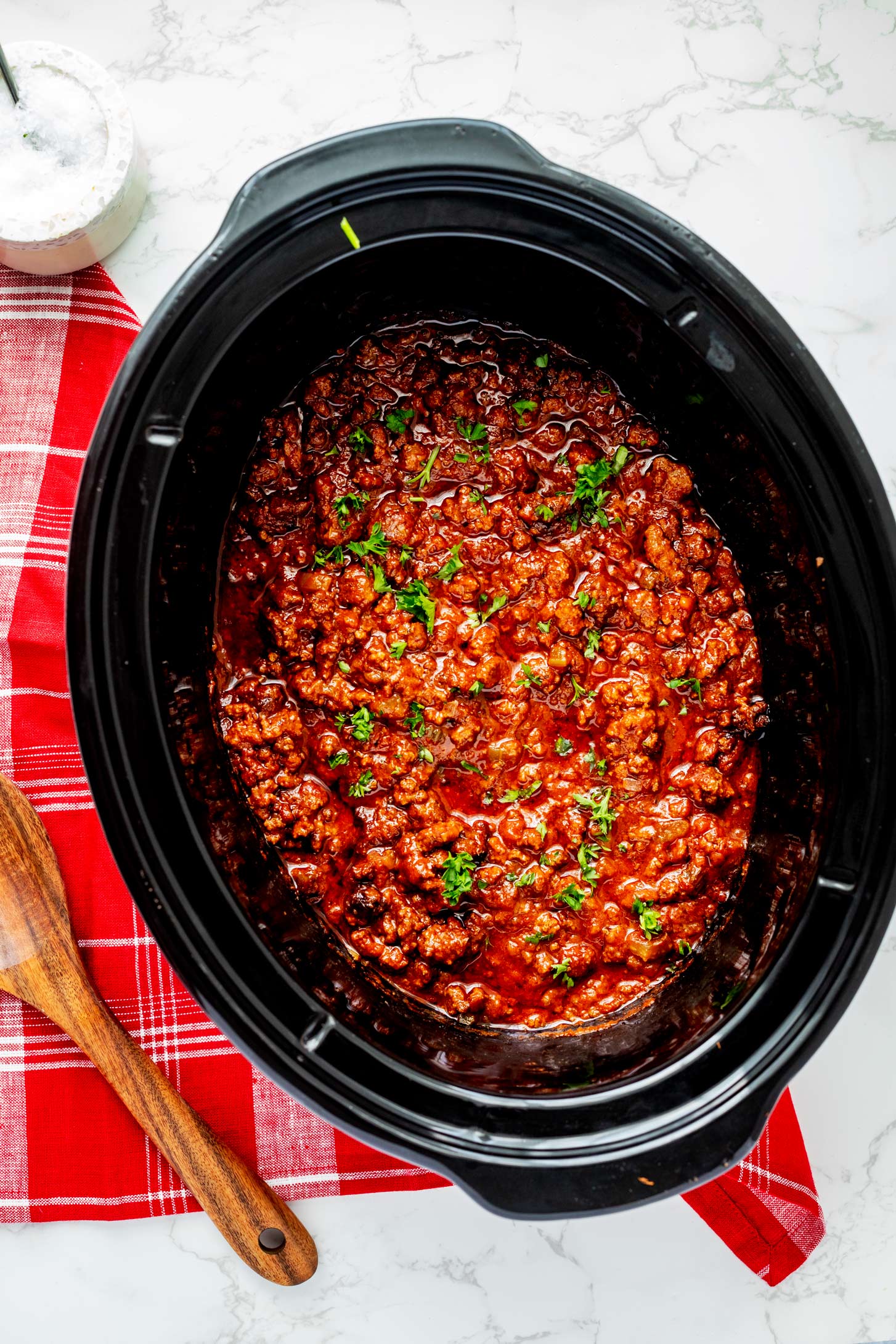 Overhead photo of slow cooker sloppy joes in a black Crockpot garnished with parsley.