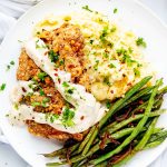 Square overhead photo of a white plate with air fryer chicken fried steak and gravy over a bed of mashed potatoes with green beans.