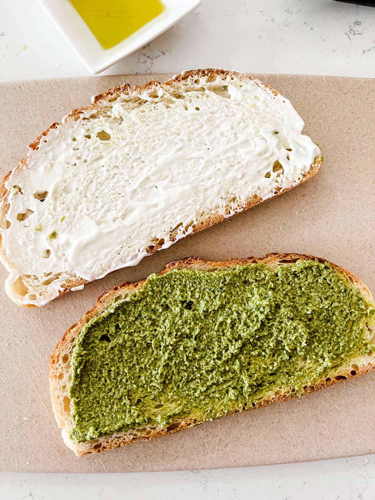 A slice of bread with mayo on it sitting next to a slice of bread with pesto.