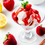 Square photo of Ninja Creami strawberry ice cream in a glass dish with strawberries and lemon.