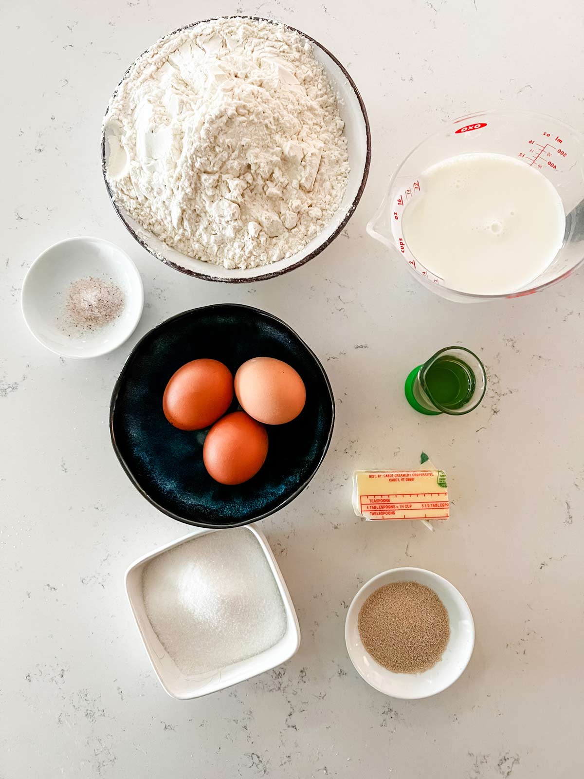 Overhead photo of flour, eggs, milk, butter, sugar, yeast, vanilla, and salt.