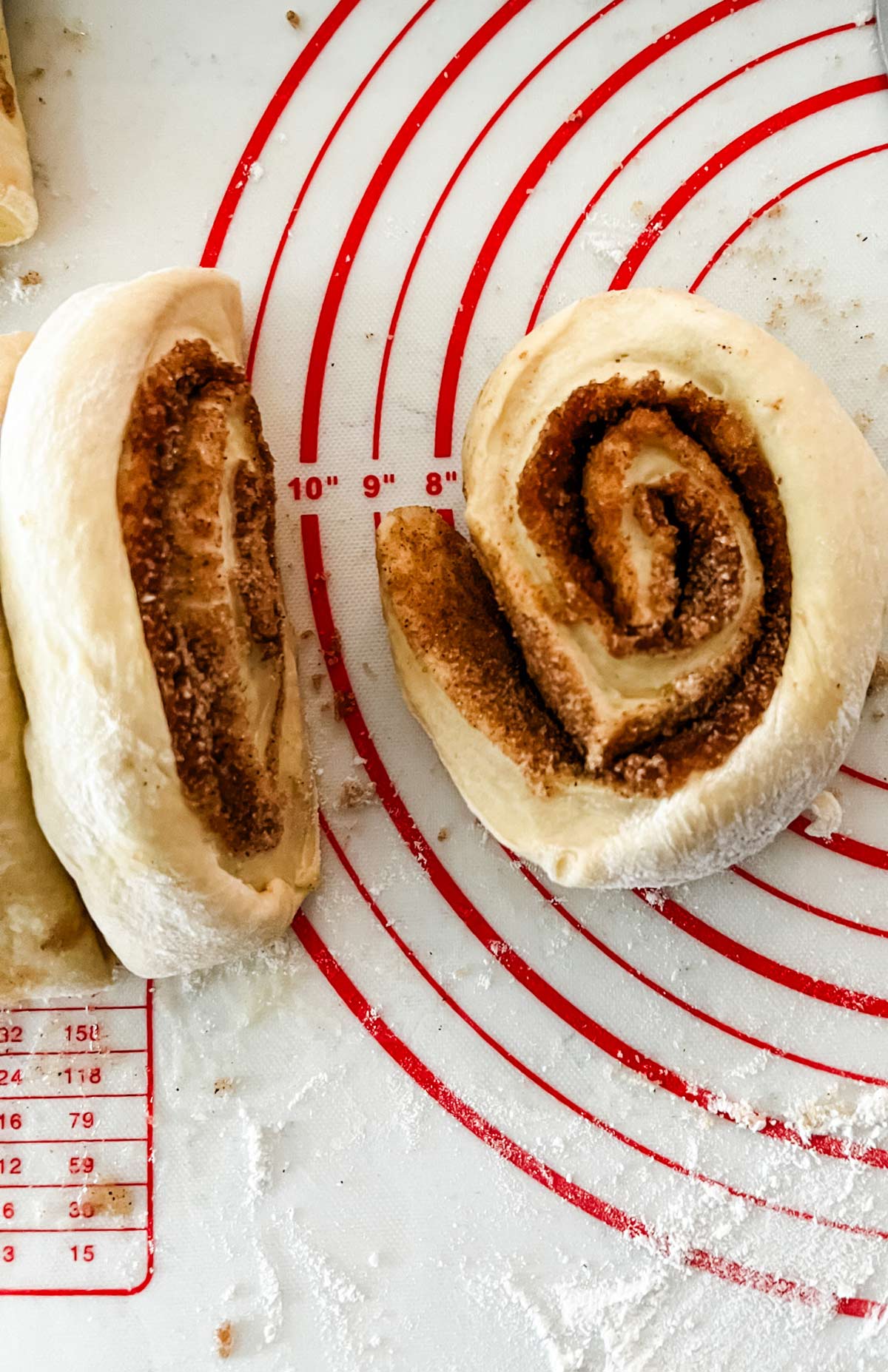 Two cut cinnamon rolls on a pastry mat.