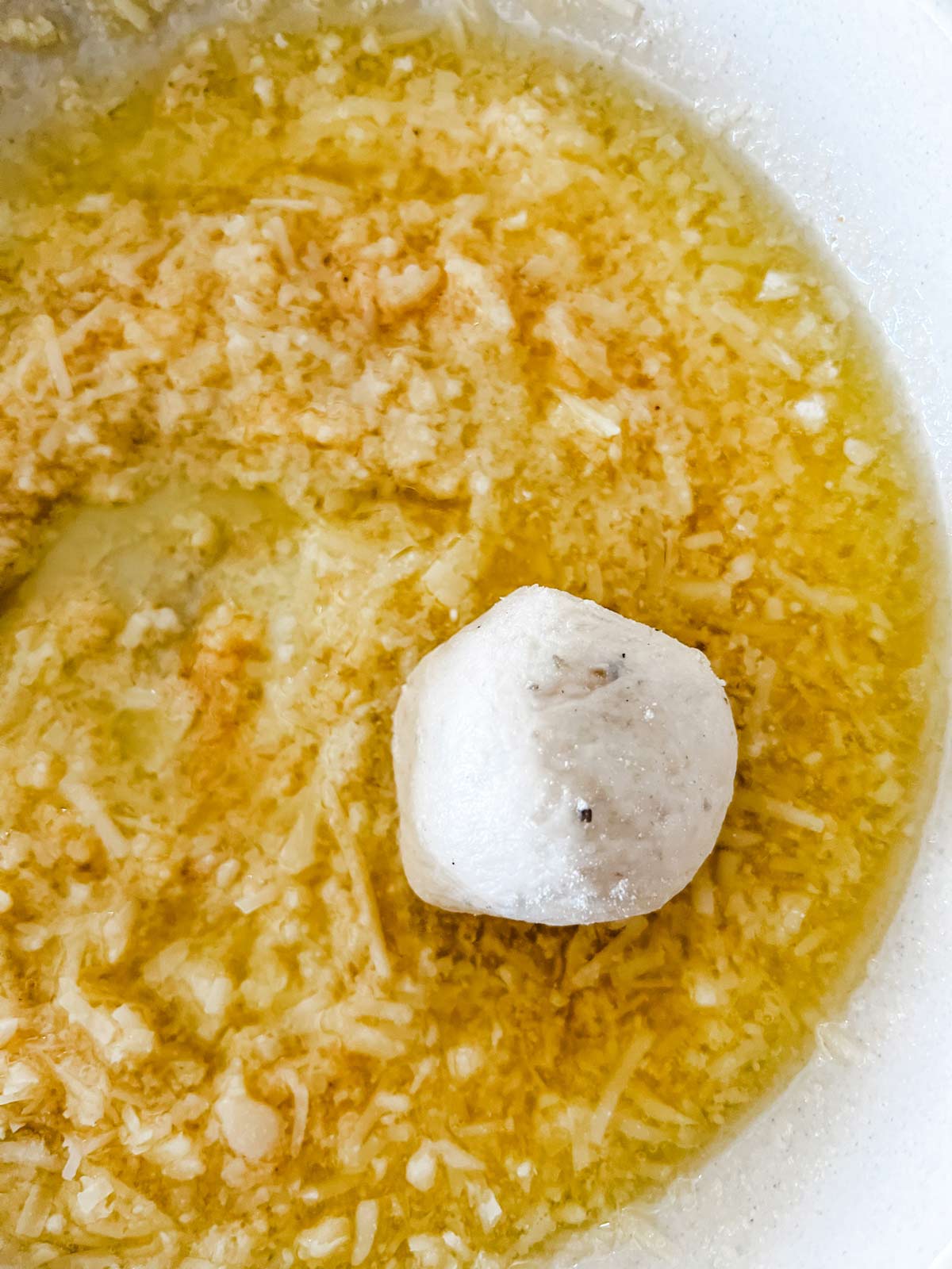A ball of bread dough being coated in a garlic parmesan mixture.