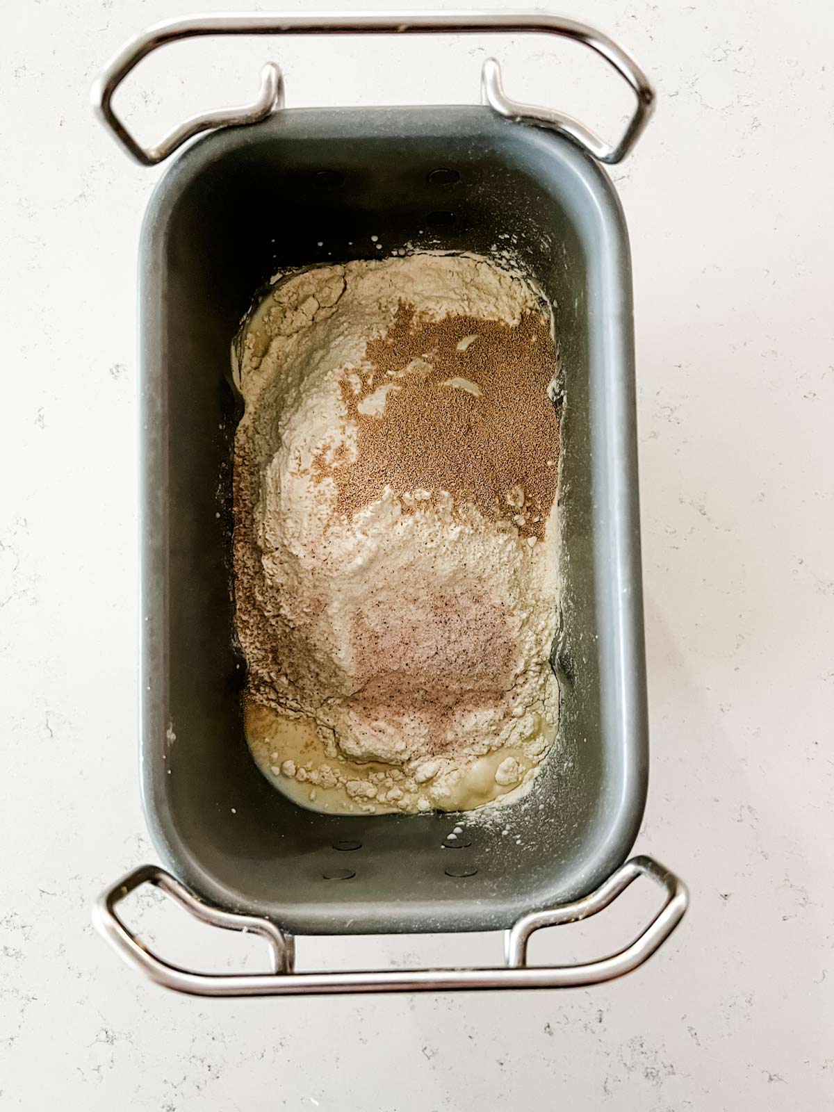 Overhead photo of milk, water, butter, honey, bread flour, yeast, and salt in a bread machine pan.