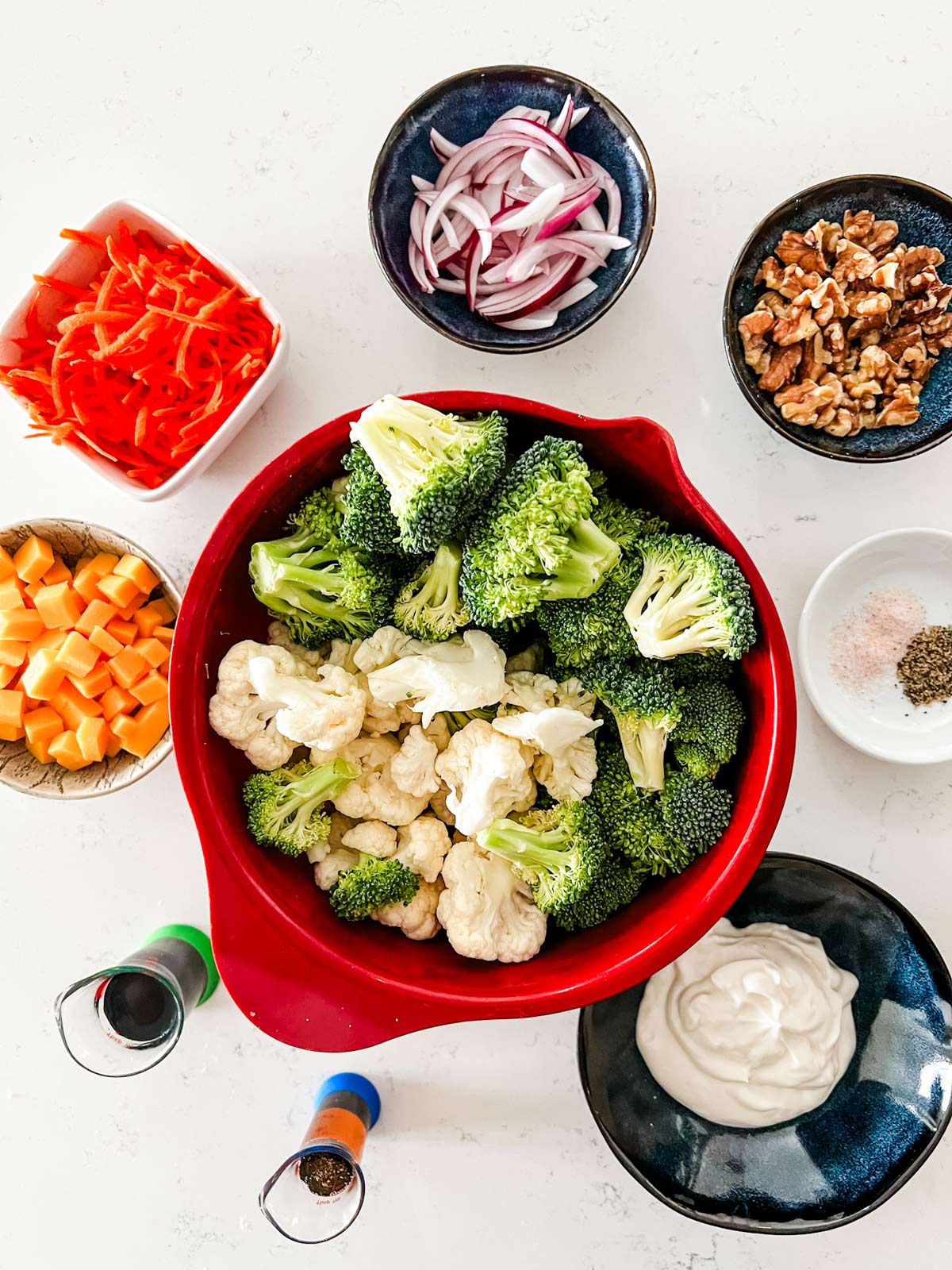 Overhead photo of broccoli, cauliflower, carrots, cheese, onion, walnuts, salt, pepper, mayo, balsamic vinegar, and maple syrup.
