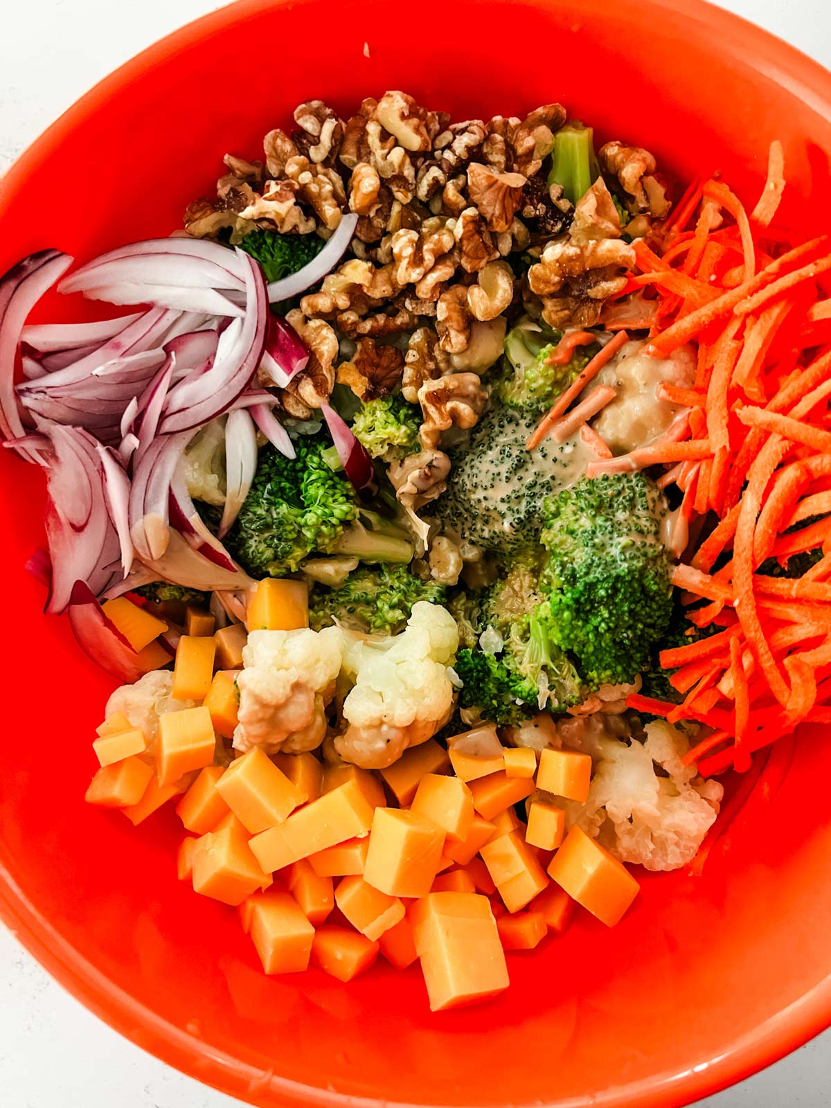 Cauliflower, broccoli, carrots, chopped cheese, onions, and walnut in a bowl with dressing.