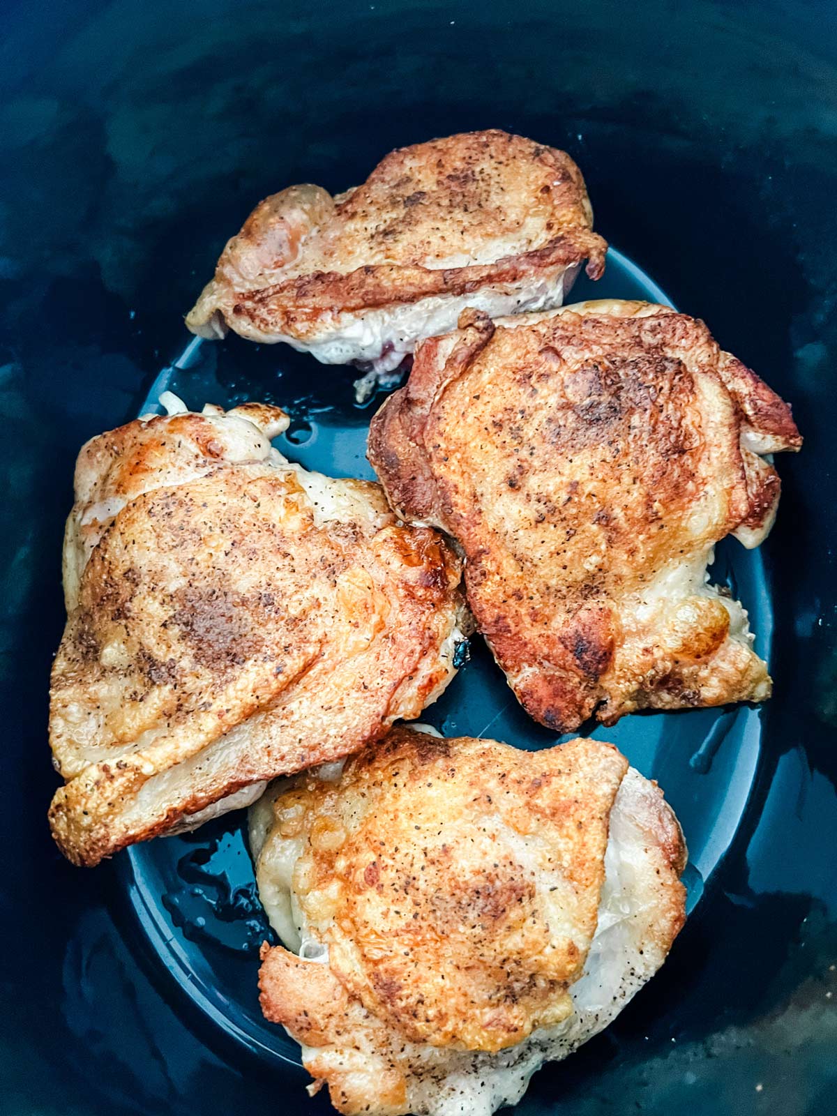Browned chicken thighs in a slow cooker.