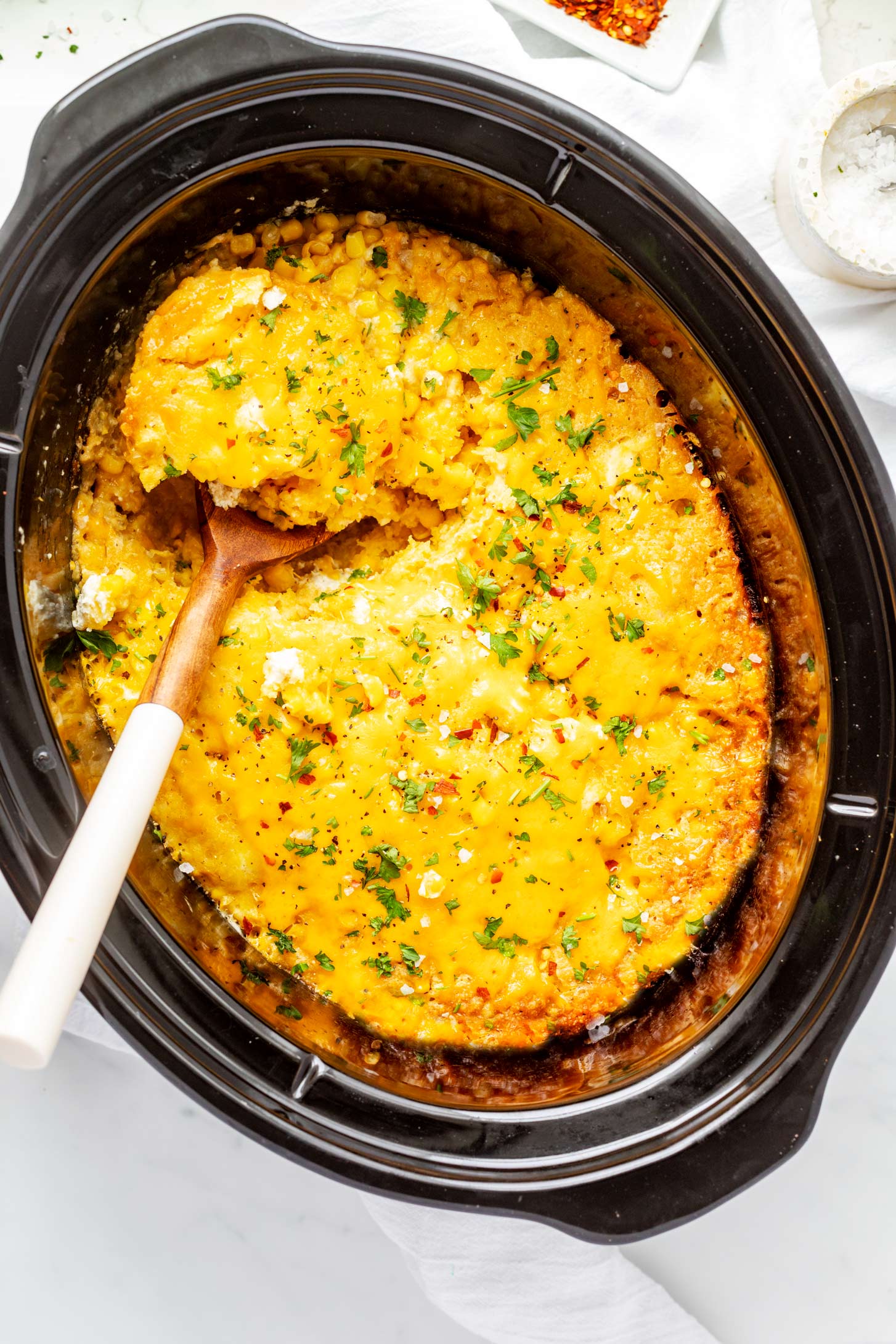 Overhead photo of crockpot corn casserole in a crockpot with a spoon dipping out a portion.