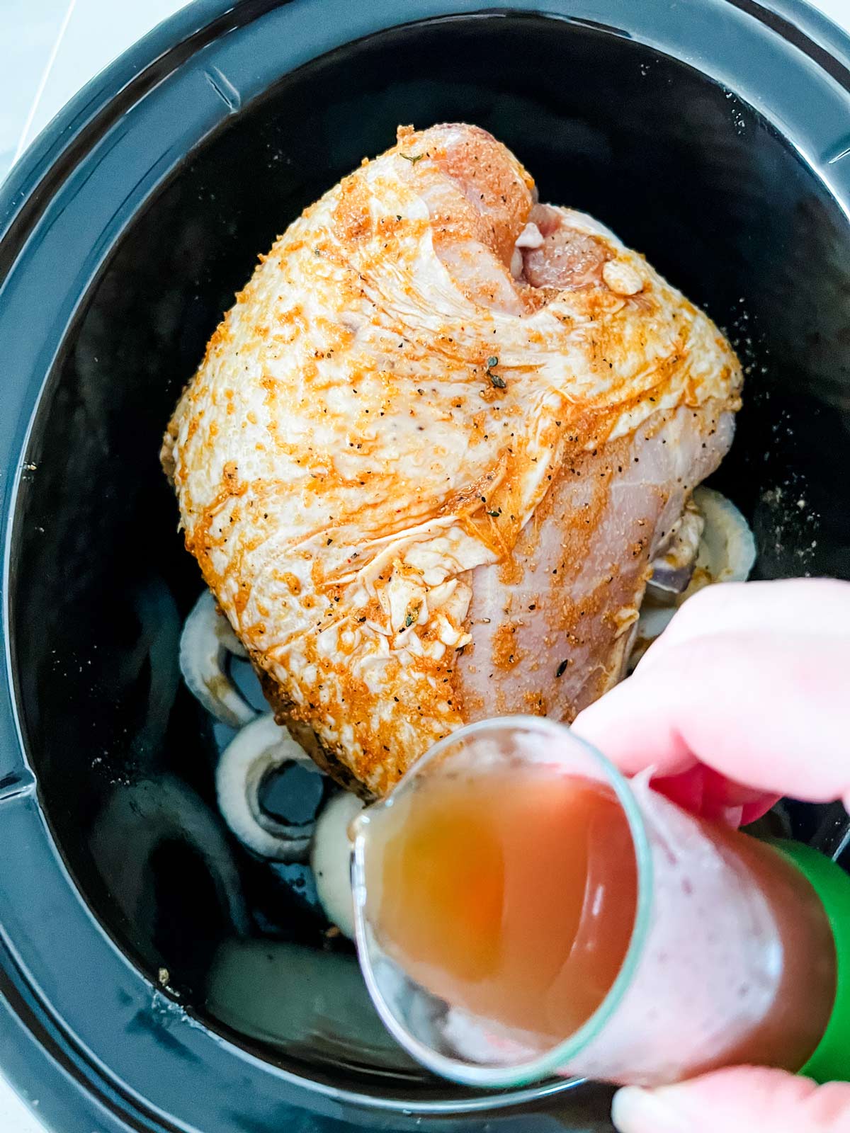 Broth being poured on a turkey breast in the slow cooker.