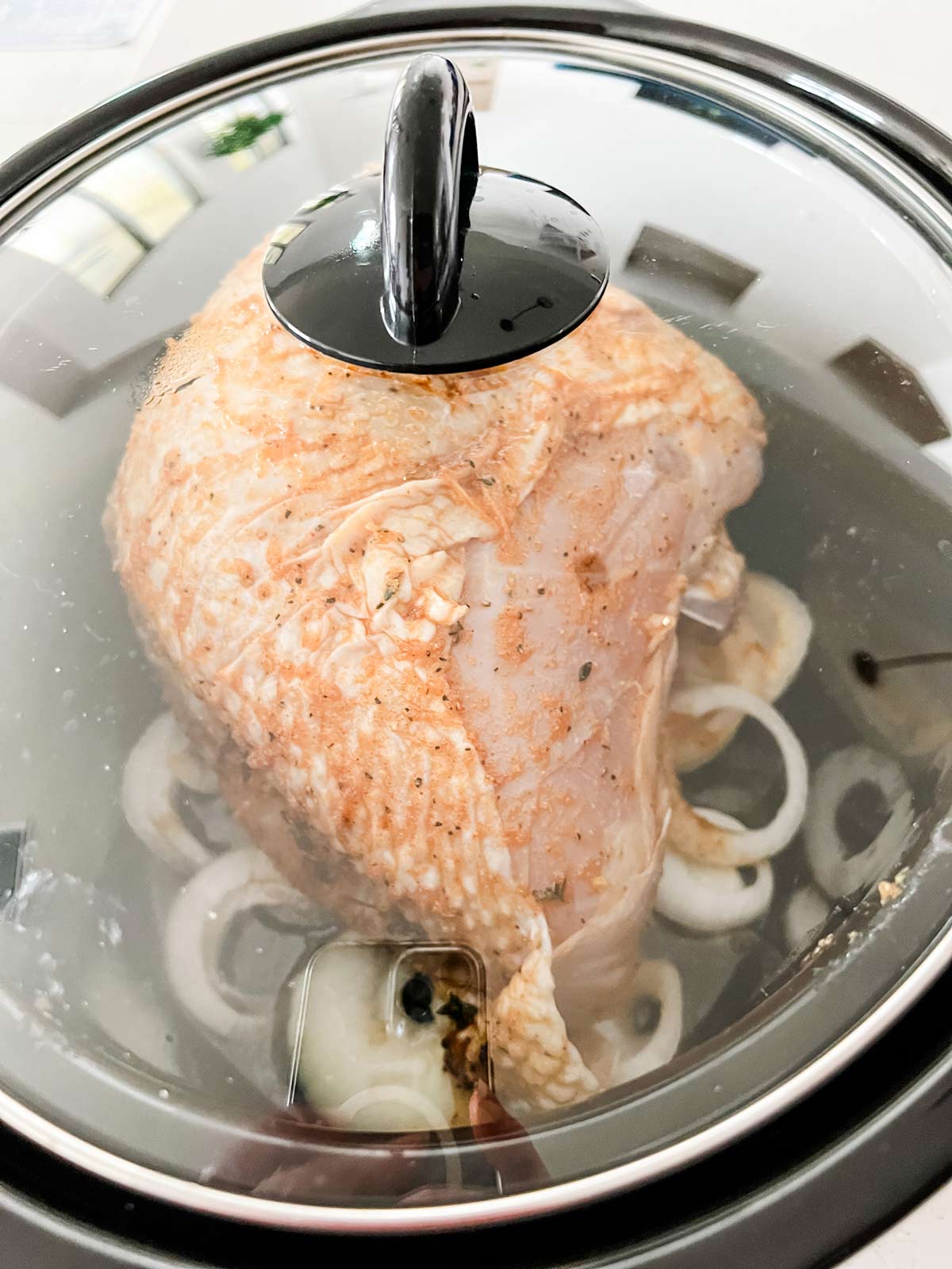 A turkey breast in a slow cooker covered and cooking.