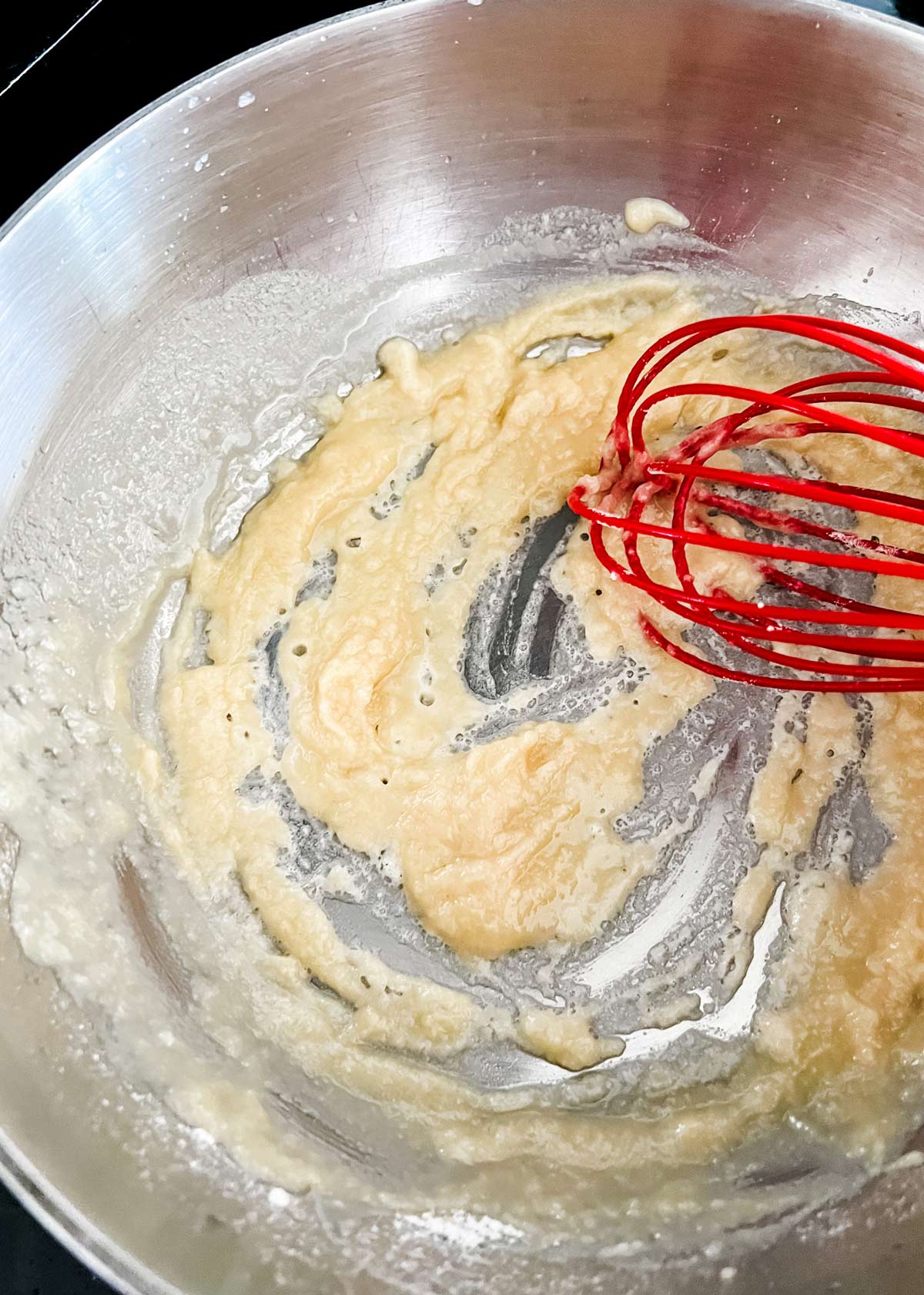 Butter in flour being whisked together in a saucepan.
