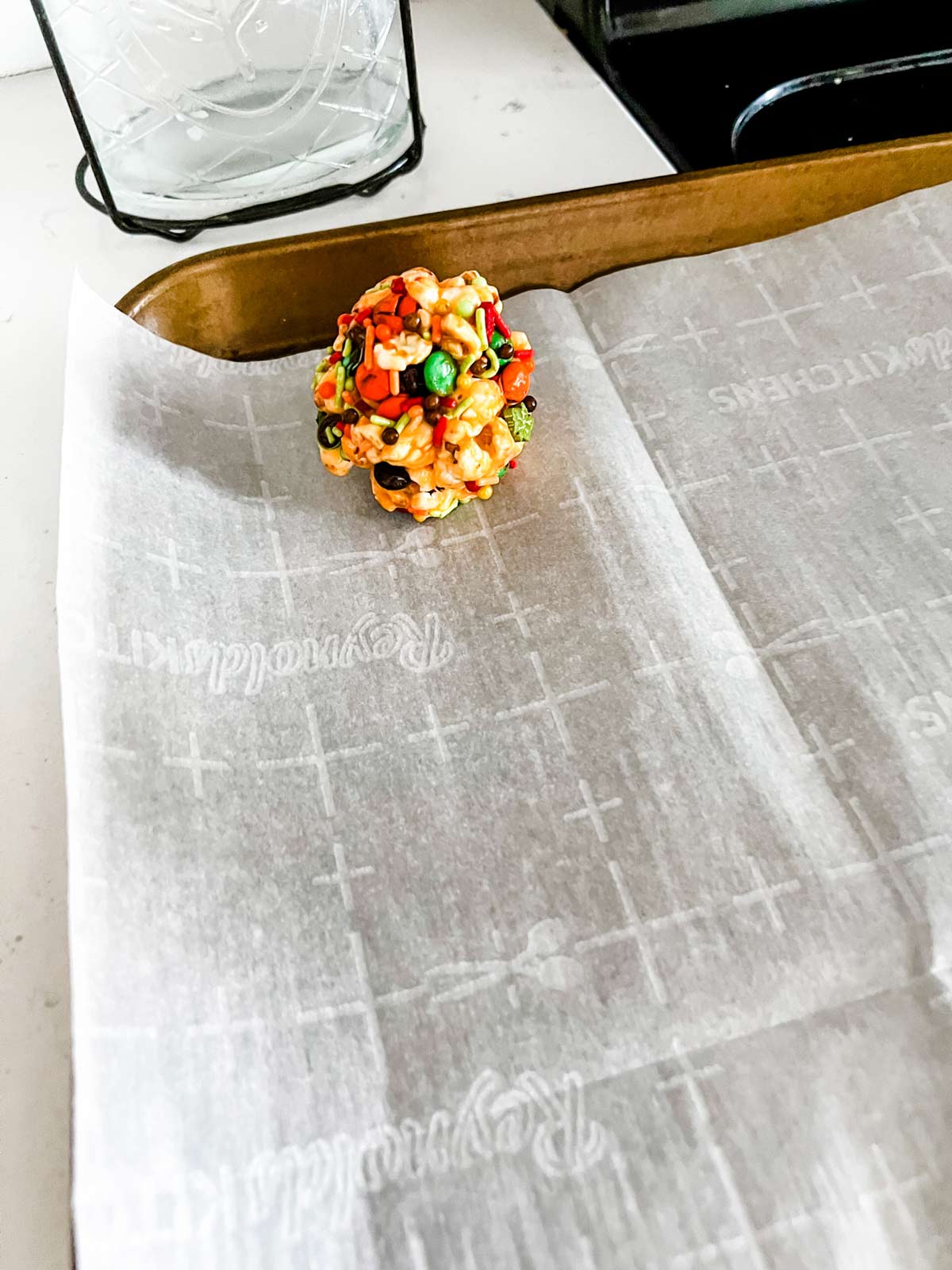 Halloween popcorn ball that has been rolled in sprinkles and placed on a parchment lined baking sheet.